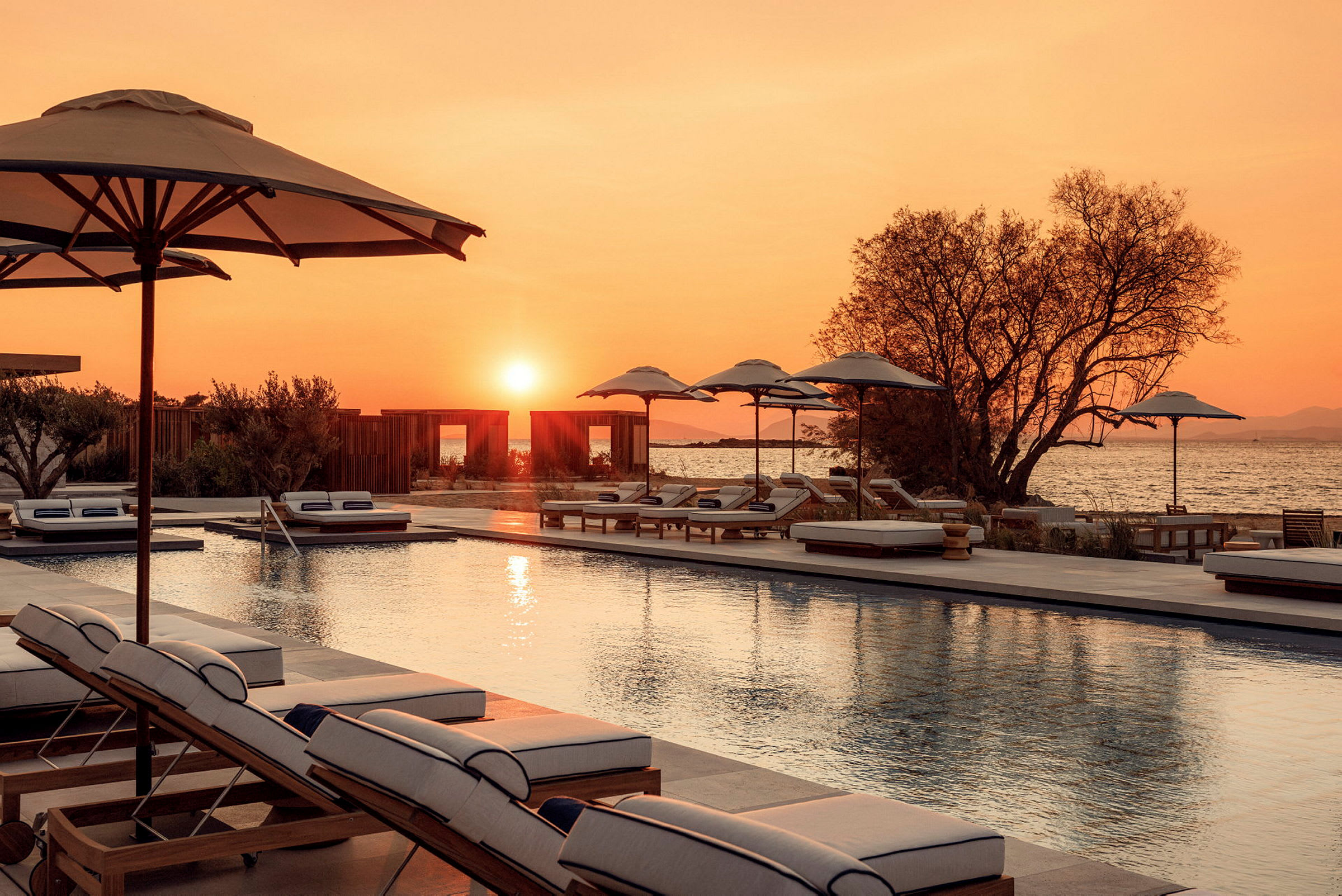 Bild av en pool med solstolar och parasoller i solnedgång vid havet. (AI-genererad text)