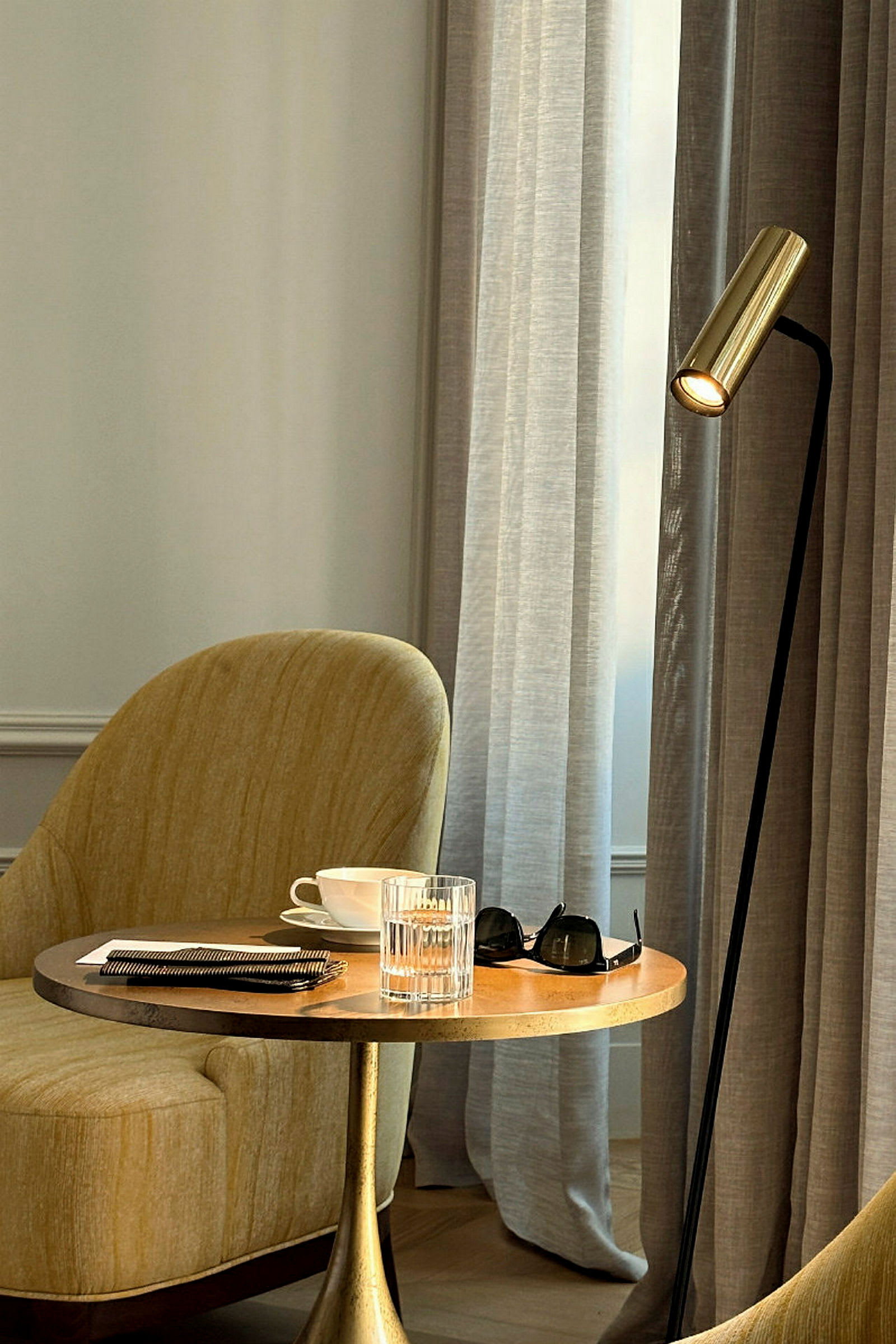 Ett bord med ett glas, en kopp och solglasögon, bredvid en gul fåtölj och en lampa. (AI-genererad text)