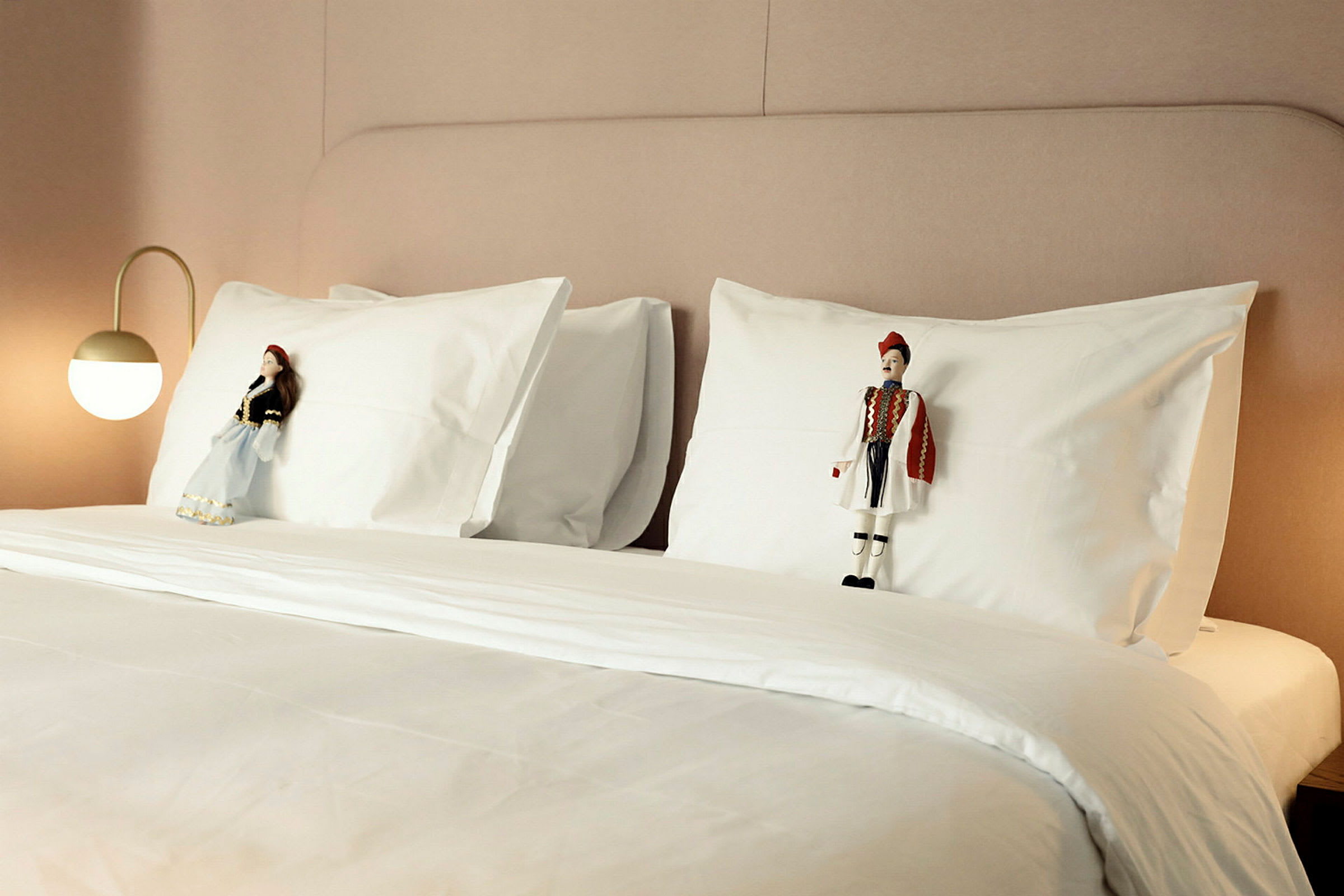 En bäddad hotellsäng med två dekorerade dockor placerade på vita kuddar. (AI-genererad text)