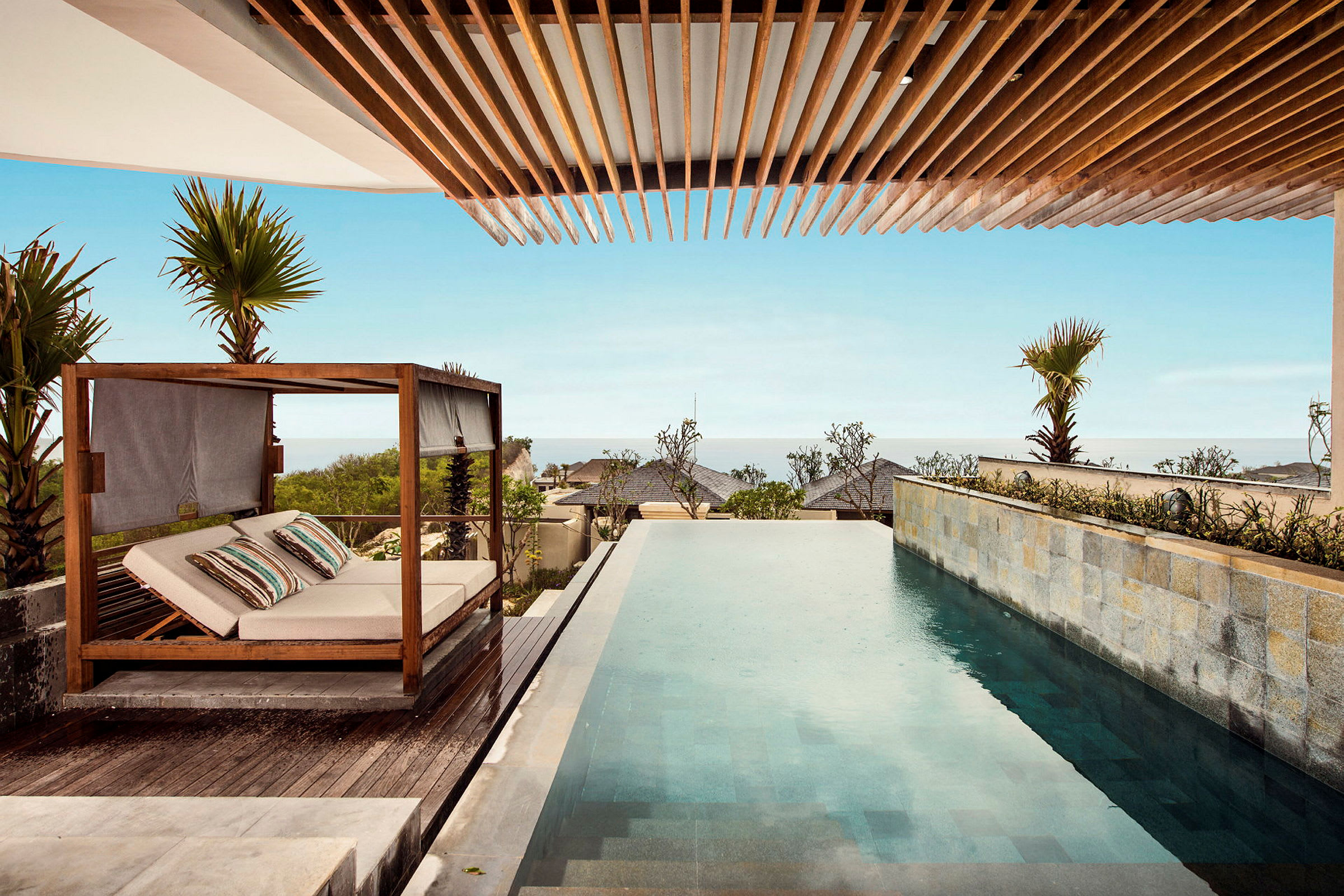 Utsikt över en infinitypool och en liggsoffa vid ett strandnära område. (AI-genererad text)