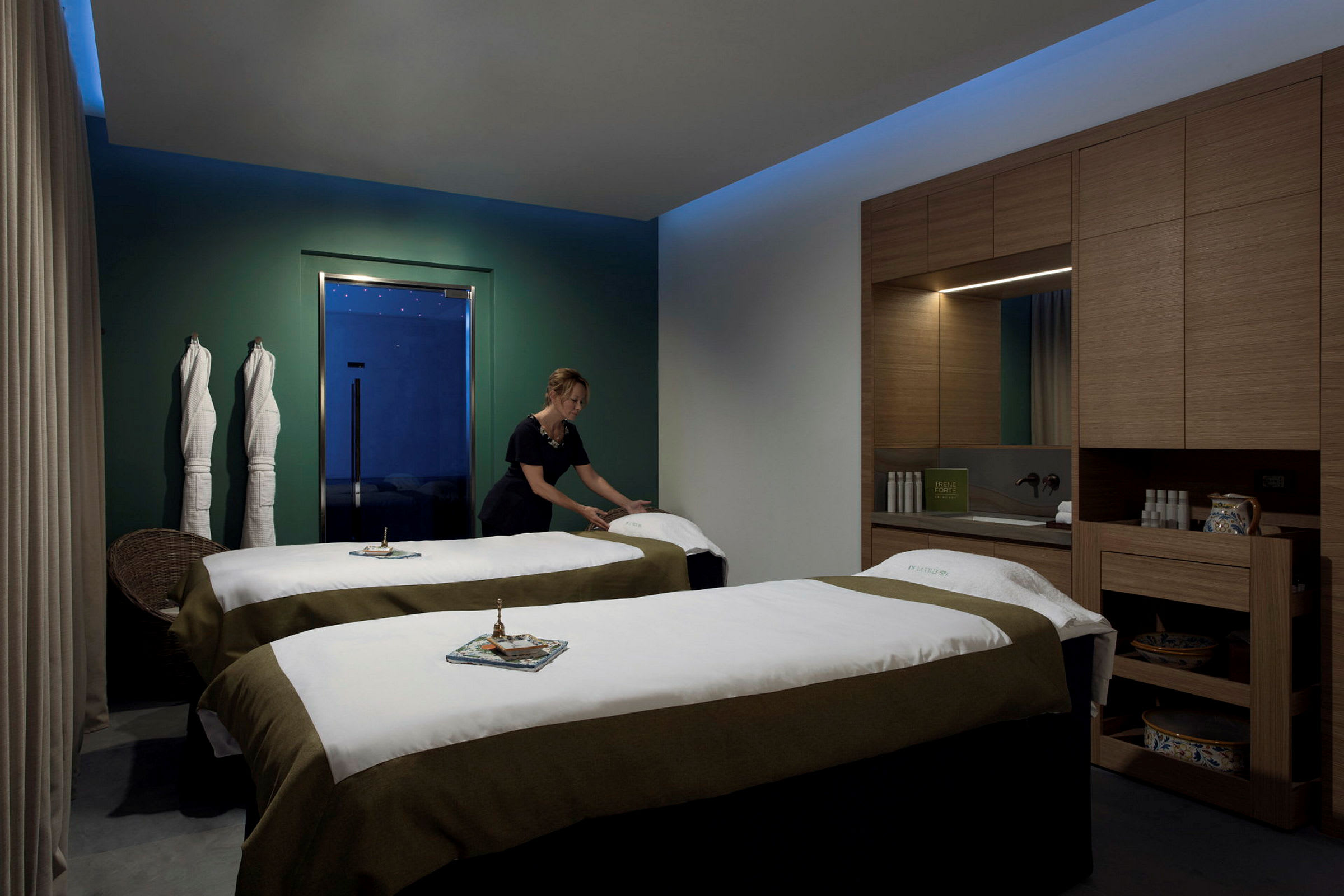 Ett spa-rum med två behandlingssängar, handdukar och hyllor fyllda med produkter. (AI-genererad text)