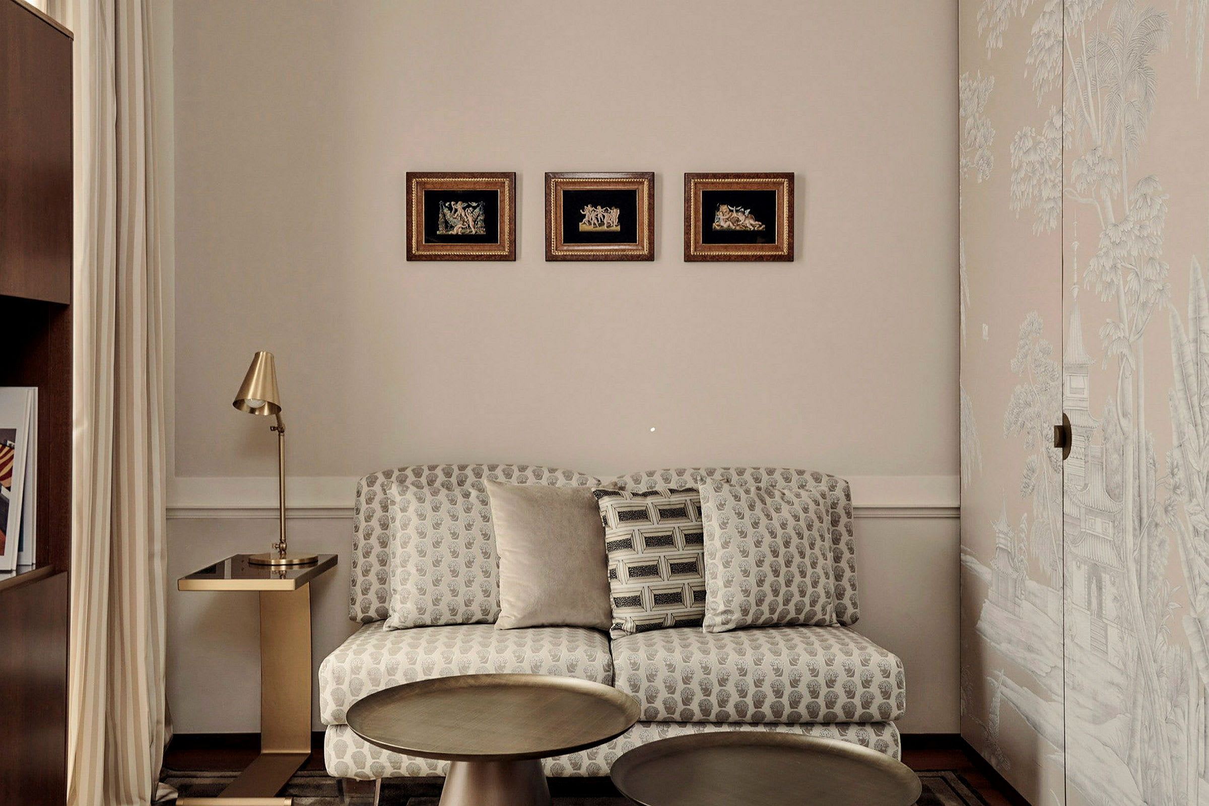 Ett rum med en soffa mot en beige vägg, en guldlampa och tre små tavlor ovanför soffan. (AI-genererad text)