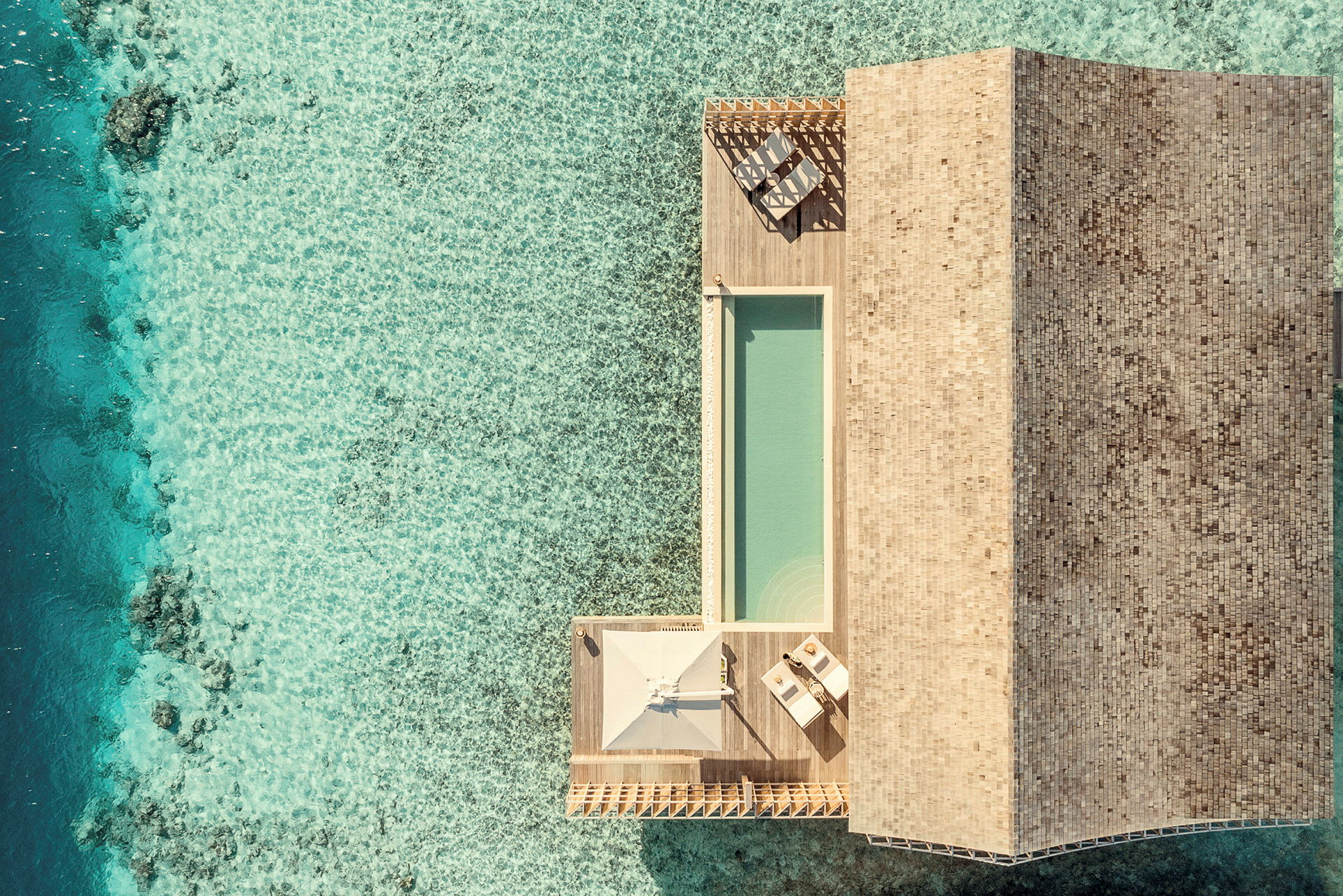 Flygbild av en övervattenvilla med terrass, pool och hav runt omkring. (AI-genererad text)