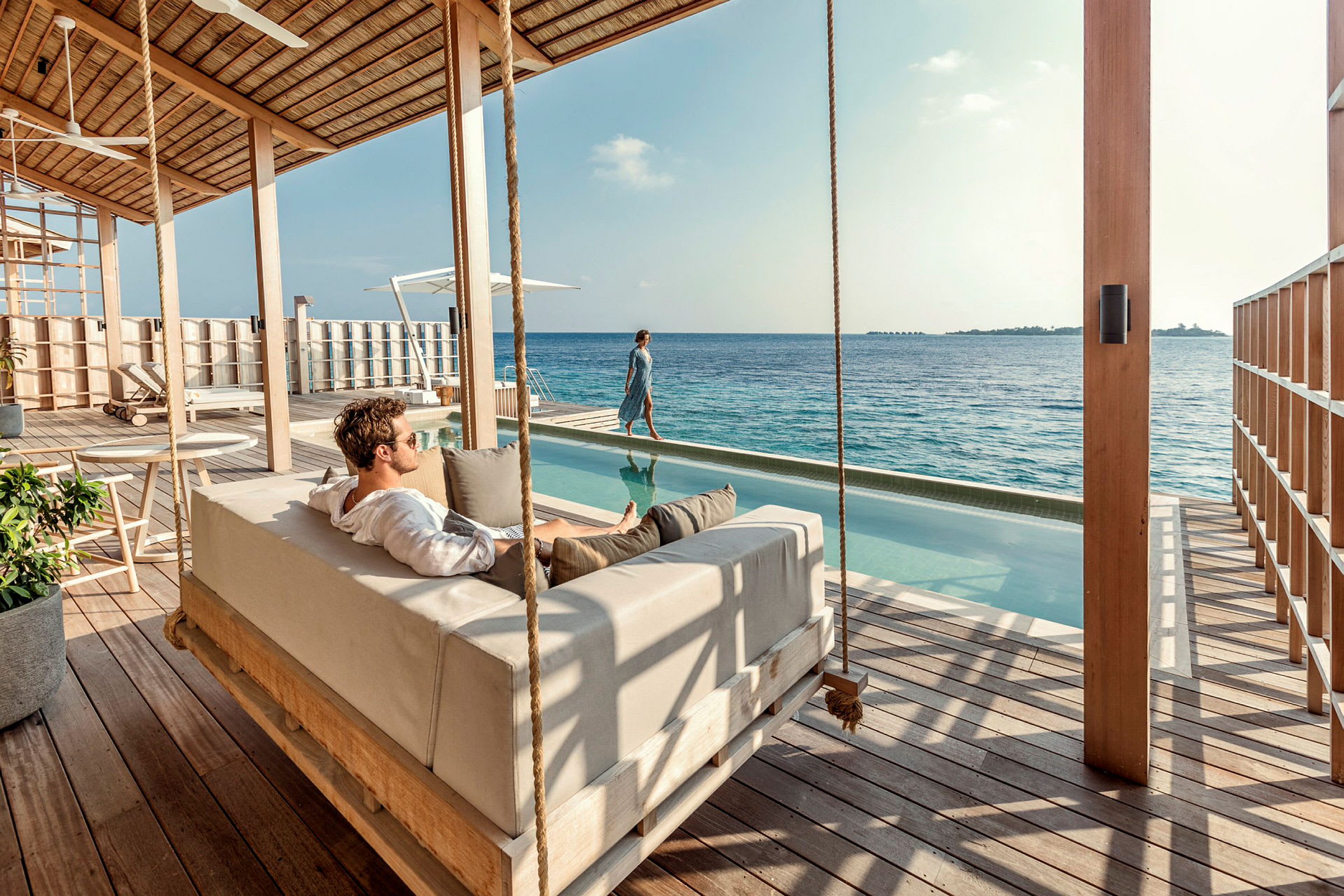 Person vilar på en hängande soffa bredvid en infinitypool vid havet. (AI-genererad text)