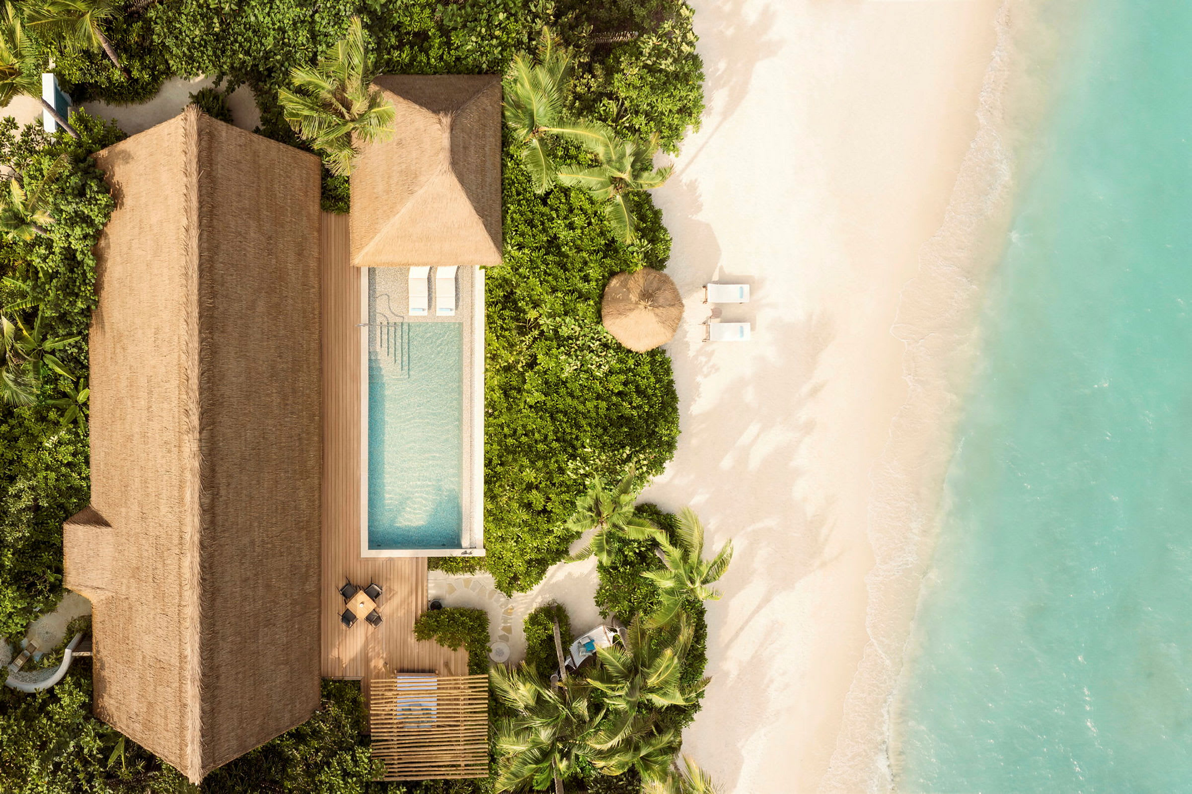 Flygfoto av en strand med transparent vatten. Ett tropiskt hus med pool och solstolar syns omgivna av grönska. (AI-genererad text)