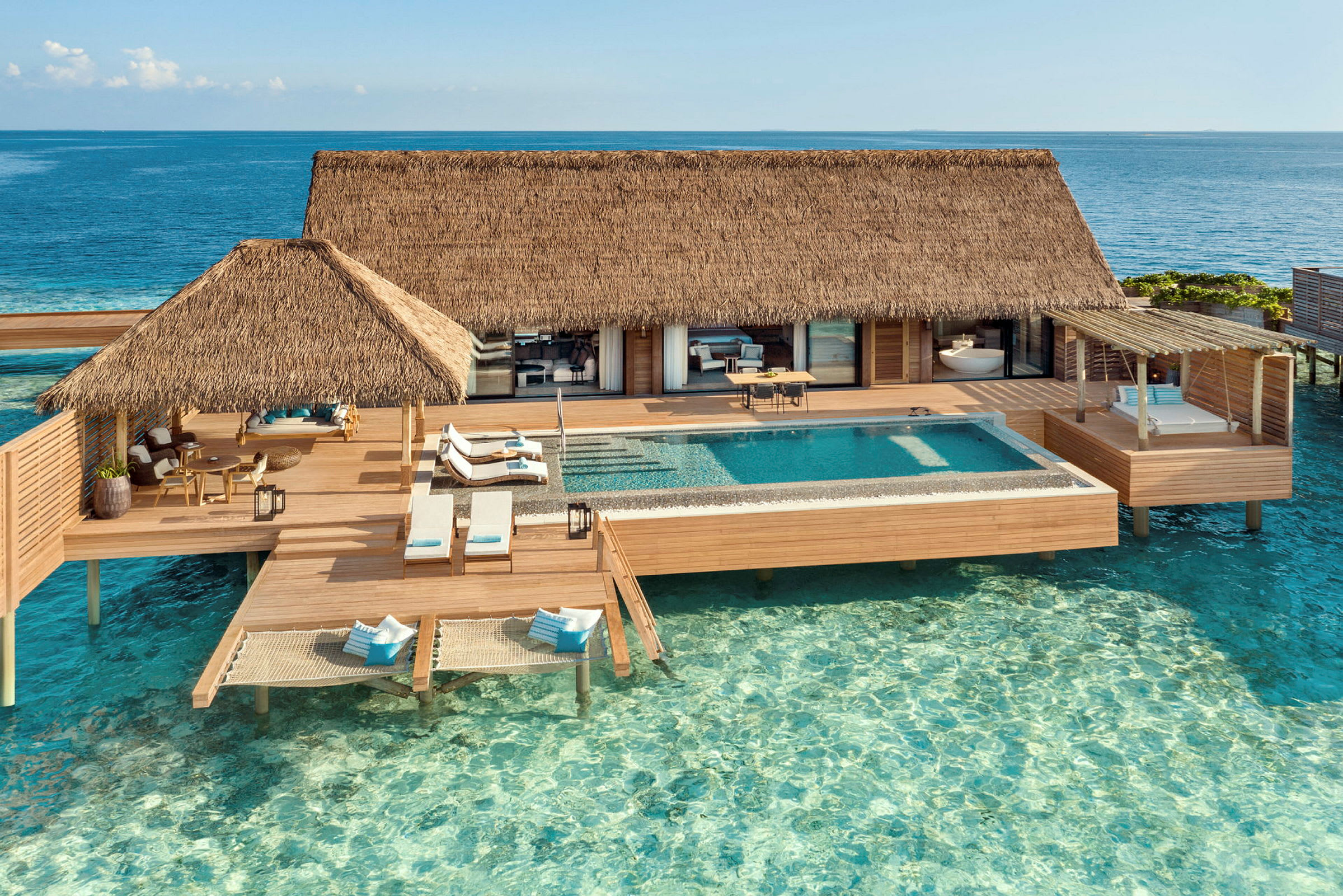 Bungalow med halmtak över vatten med soldäck och pool. (AI-genererad text)