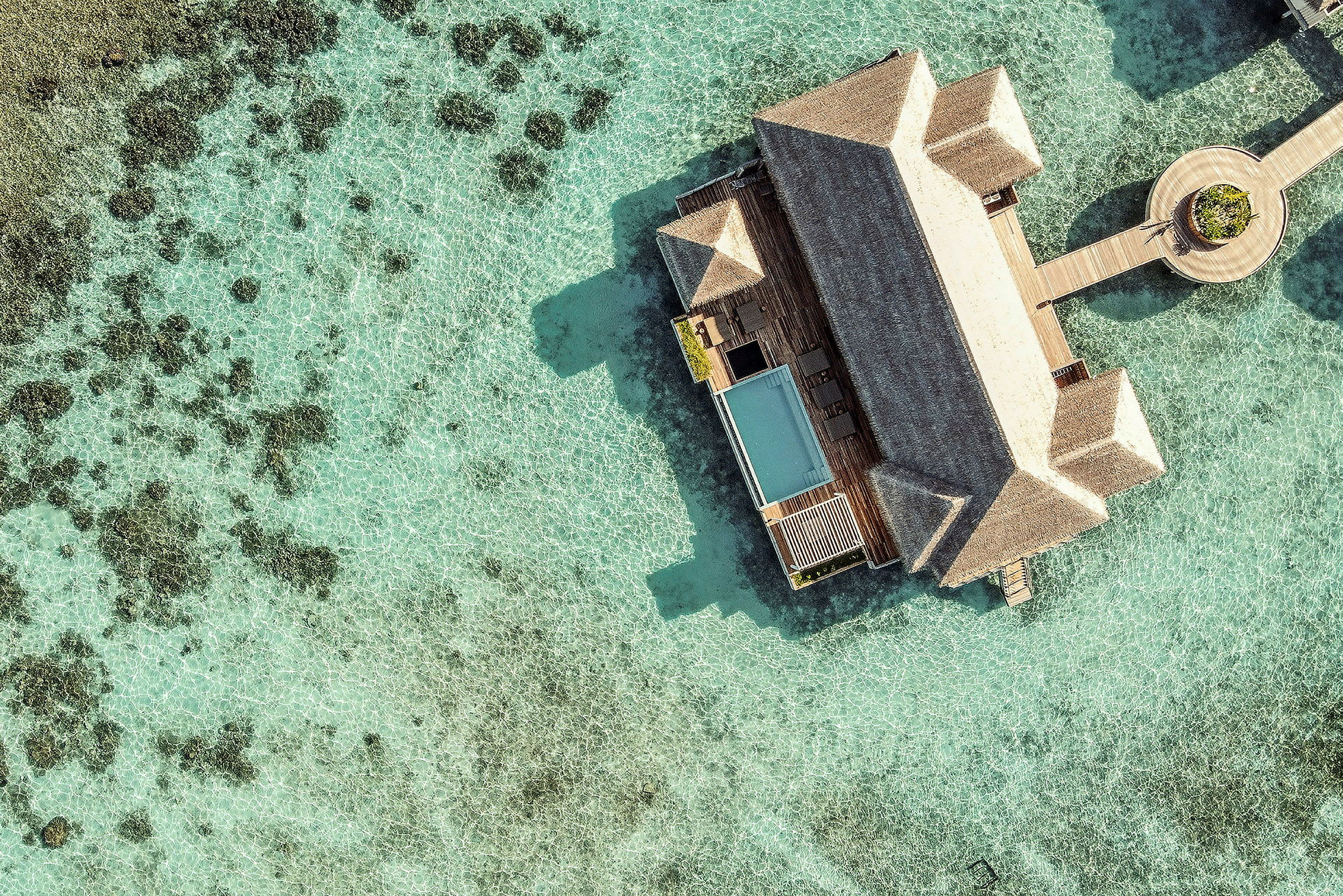 Flygfoto av en lyxig bungalow med pool på vattnet, omgiven av klart blått hav. (AI-genererad text)