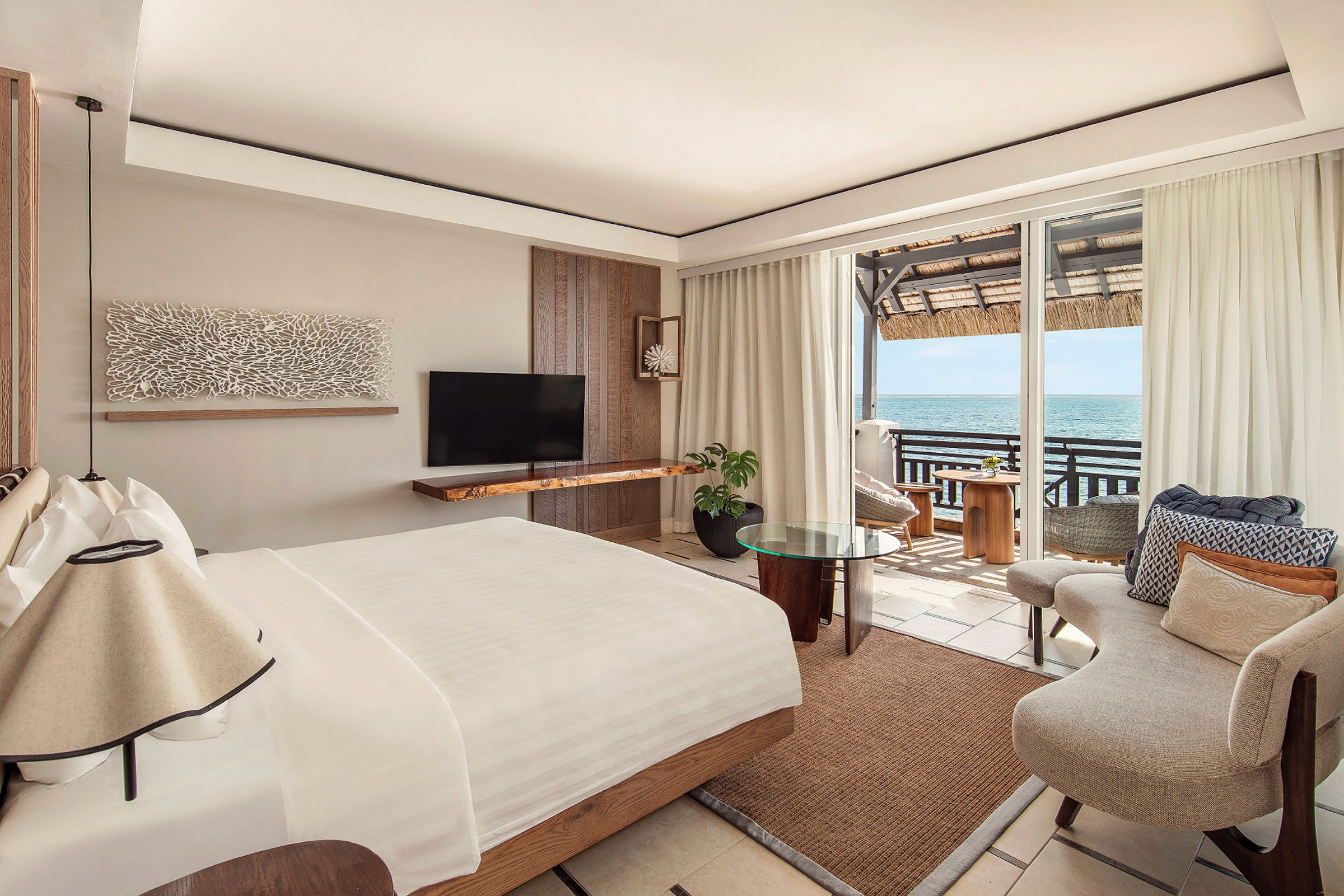 Ett elegant hotellrum med en stor säng, en fåtölj och utsikt över havet från en balkong. (AI-genererad text)