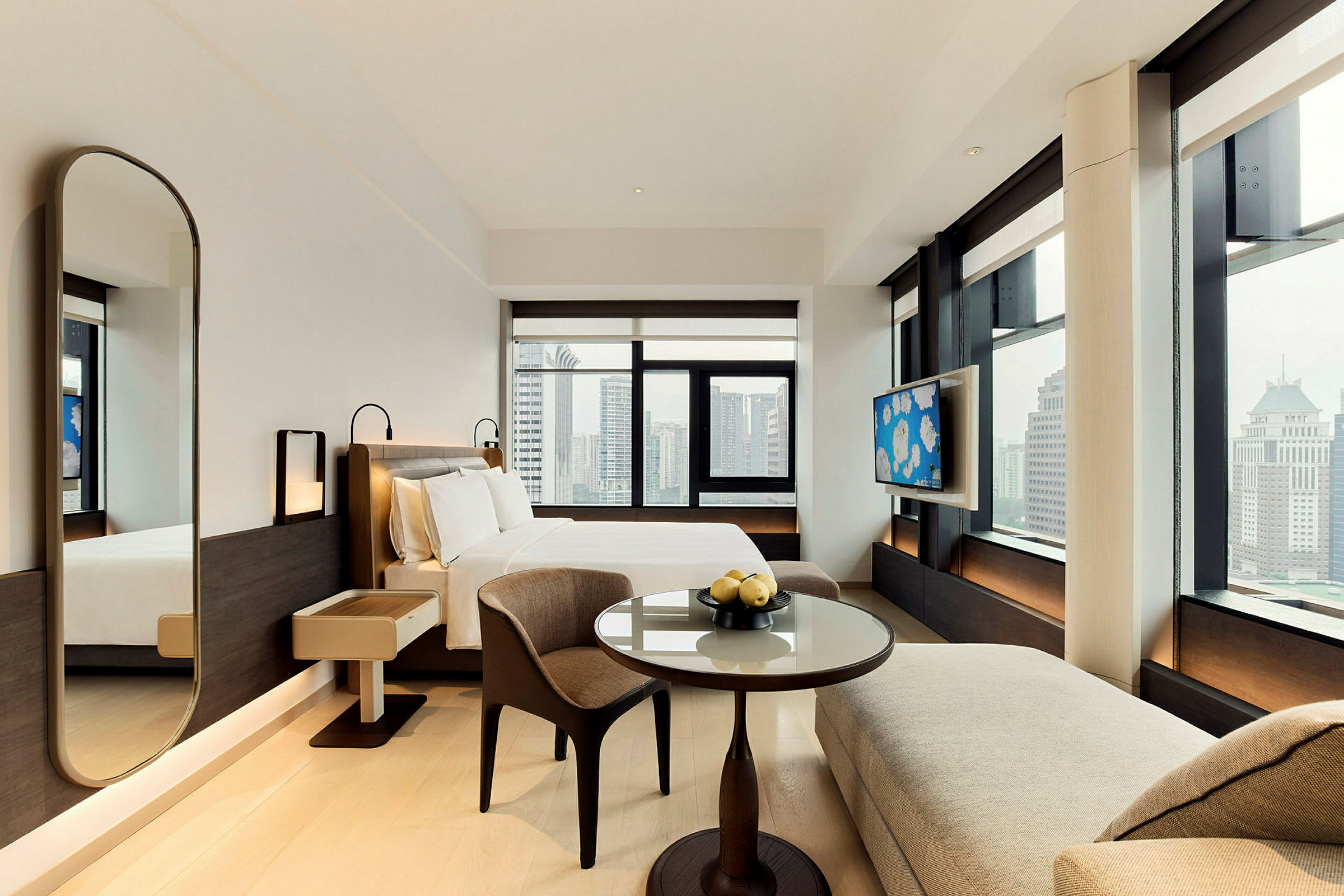 En modern hotellsvit med en dubbelsäng, ett runt bord och utsikt över staden från stora fönster. (AI-genererad text)