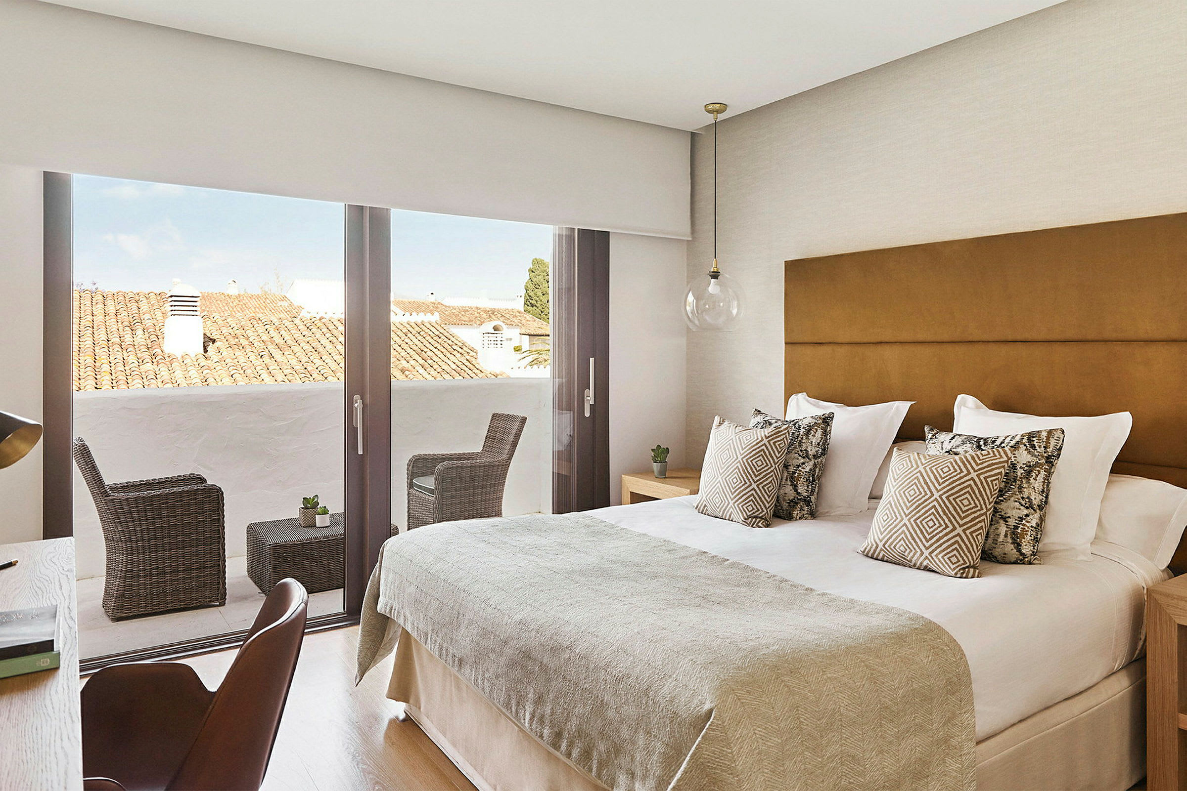 Bild på ett hotellrum med dubbelsäng, dekorerade kuddar och en terrass med sittmöbler. (AI-genererad text)