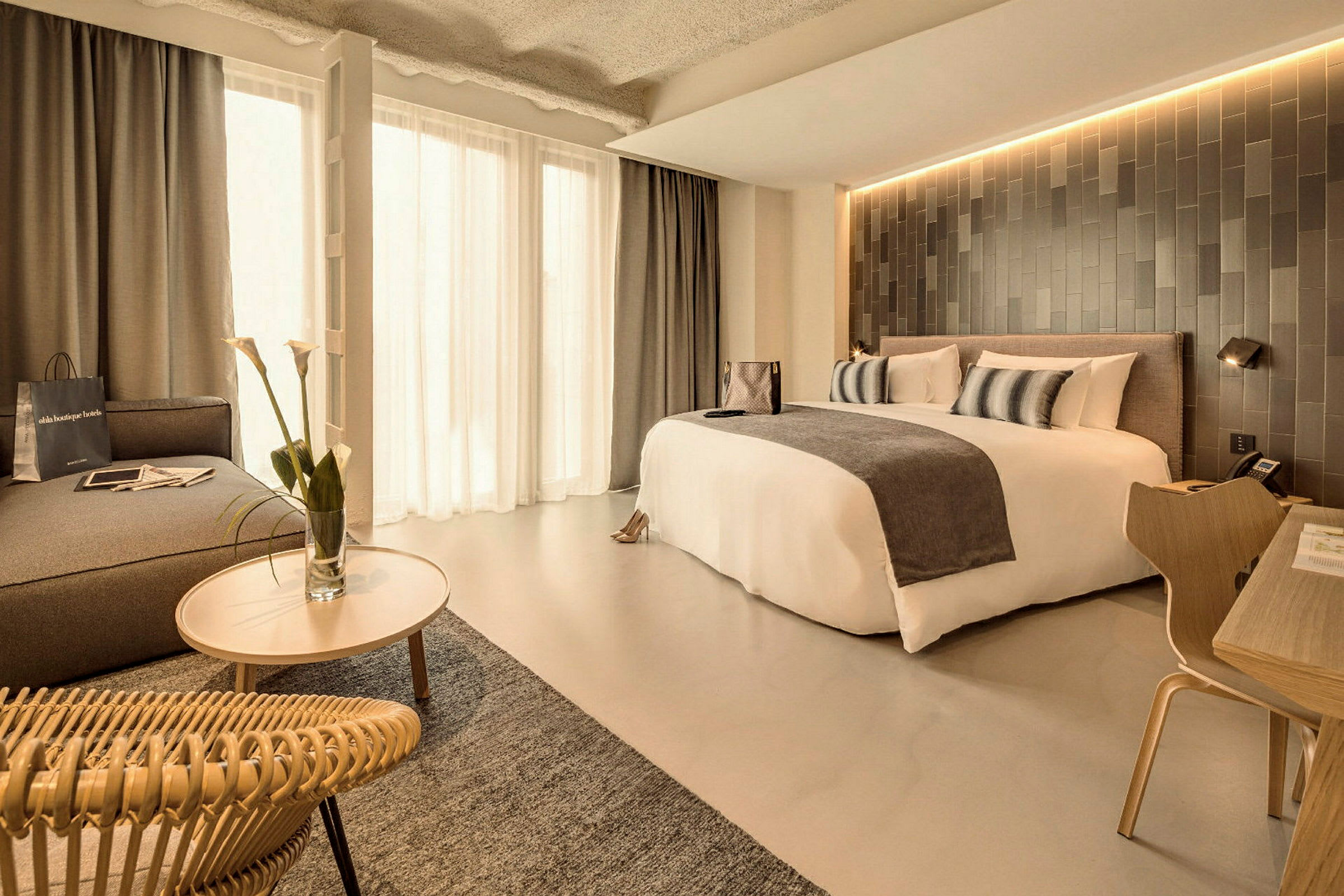 Ett modernt hotellrum med en stor säng, bord och stol samt sittgrupp med blommor. (AI-genererad text)
