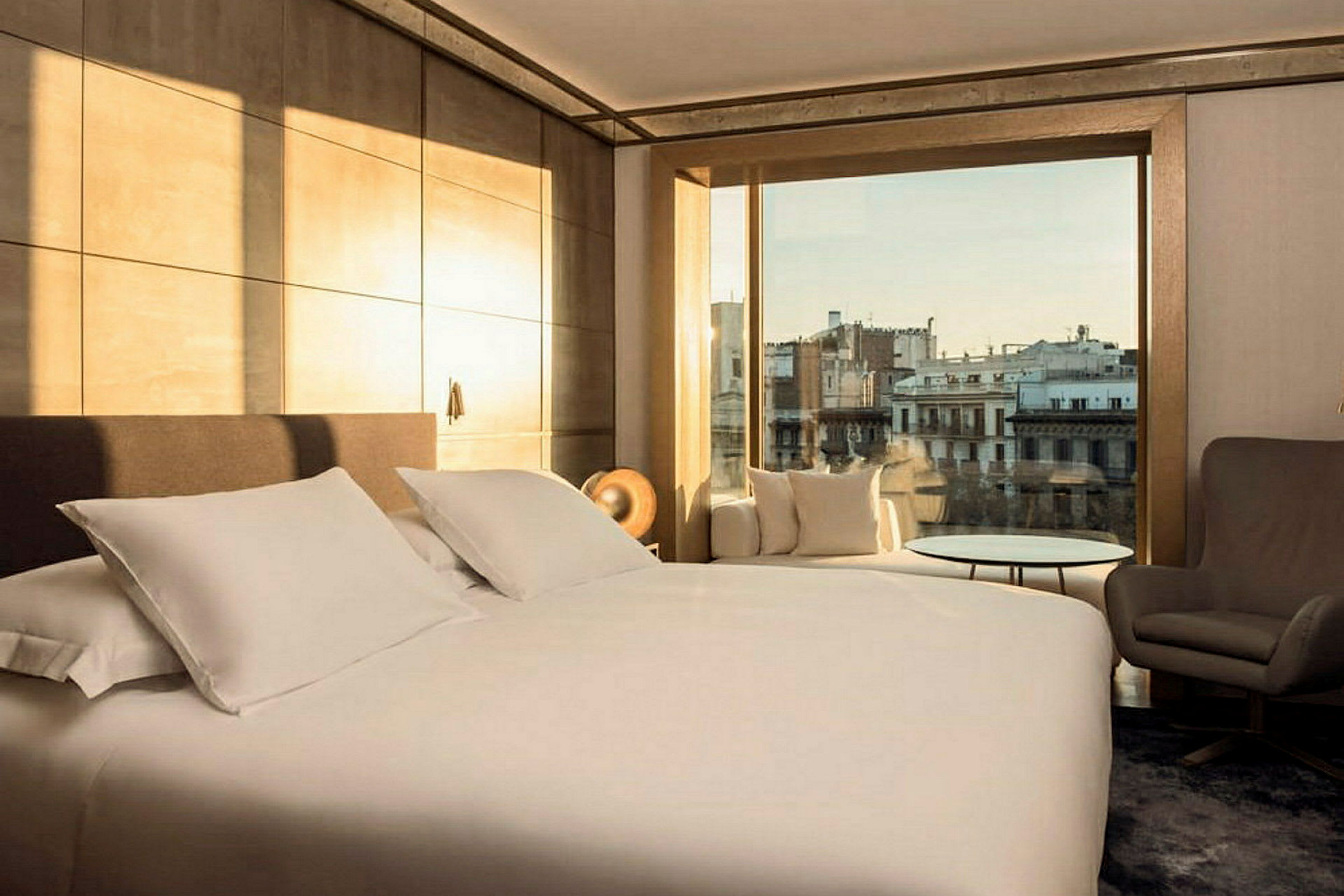 Hotellrum med en stor säng, fåtölj och utsikt över en stad. (AI-genererad text)