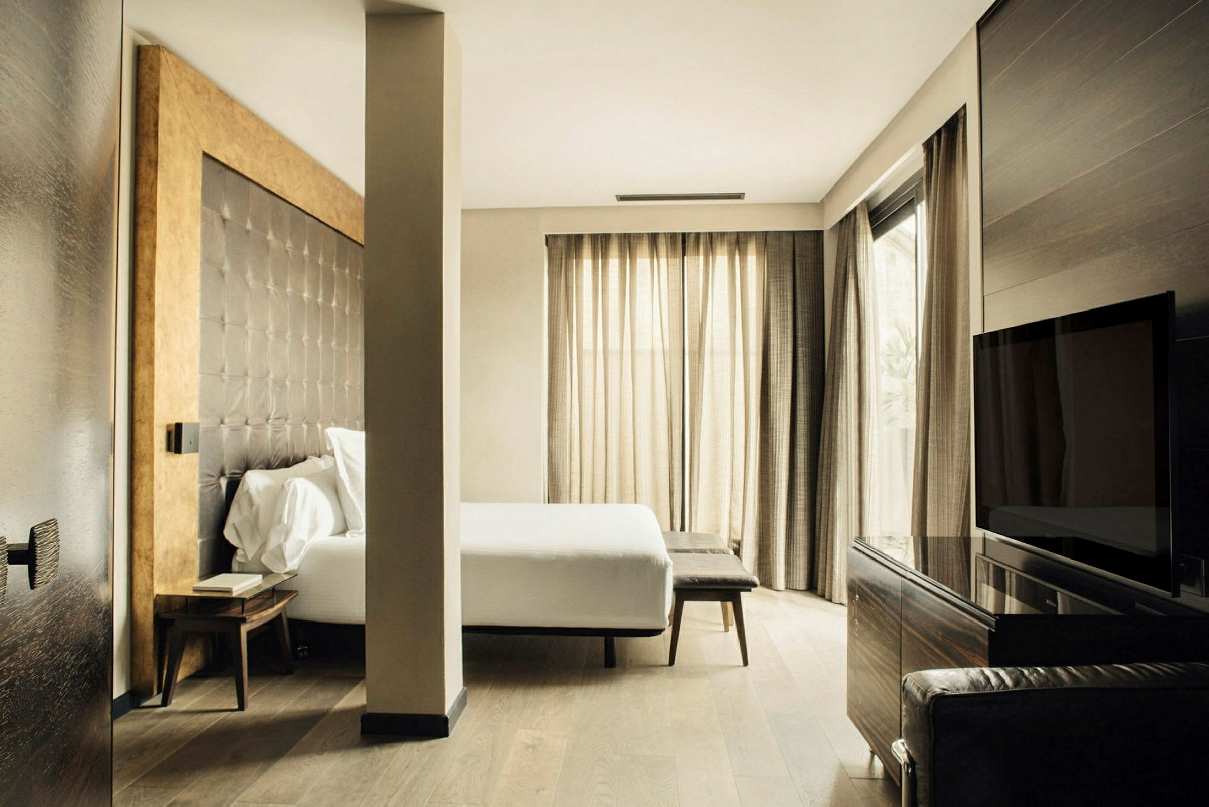 Ett modernt hotellrum med en stor säng, sittmöbler och stora fönster med ljusa gardiner. (AI-genererad text)