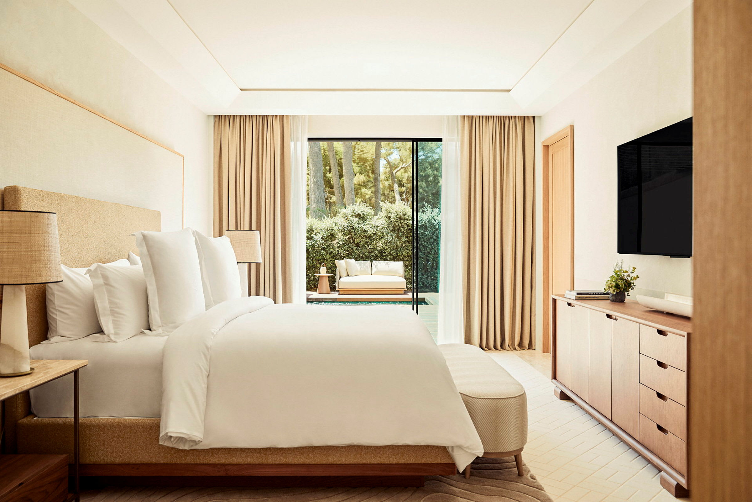 Ett modernt hotellrum med en dubbelsäng, en TV på väggen och ett stort fönster med utsikt mot en möblerad terrass och grönska. (AI-genererad text)