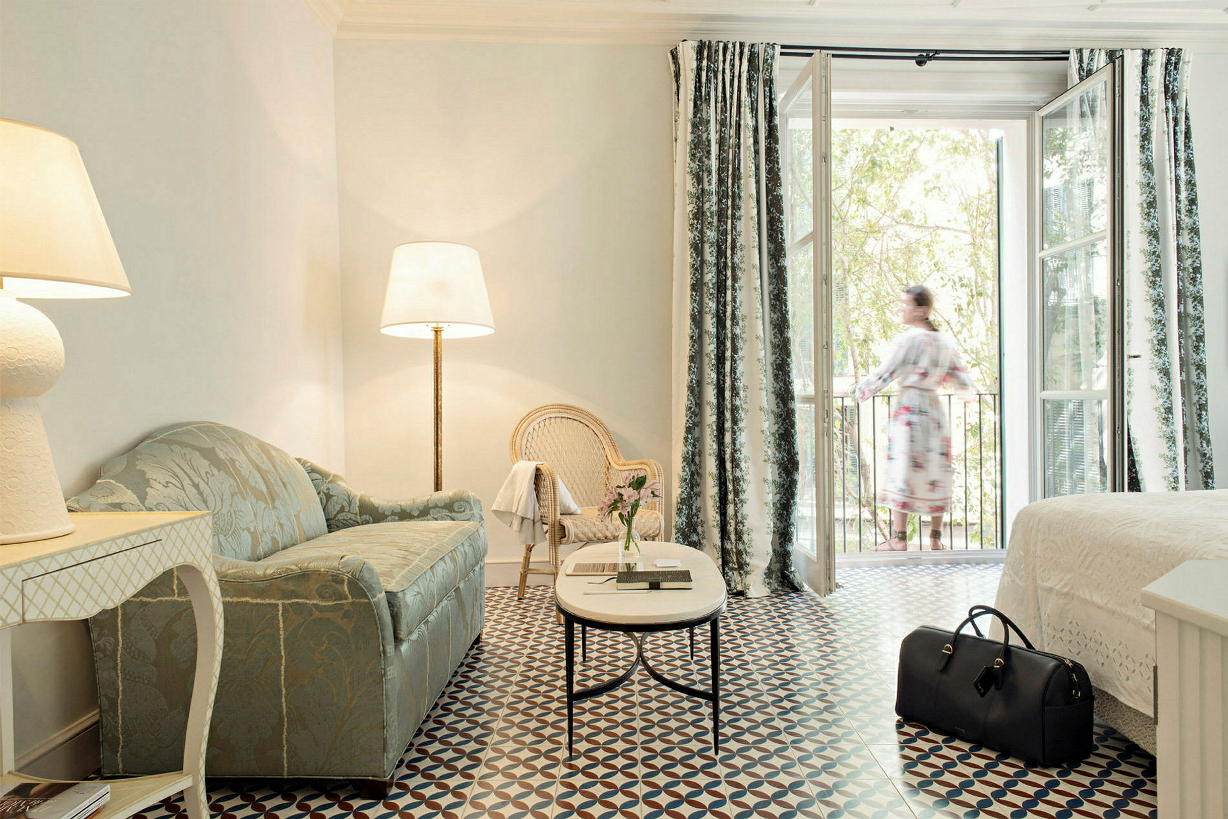 Elegant hotellrum med en soffa, fåtölj, golvlampa och bord på mönstrad golvyta. (AI-genererad text)