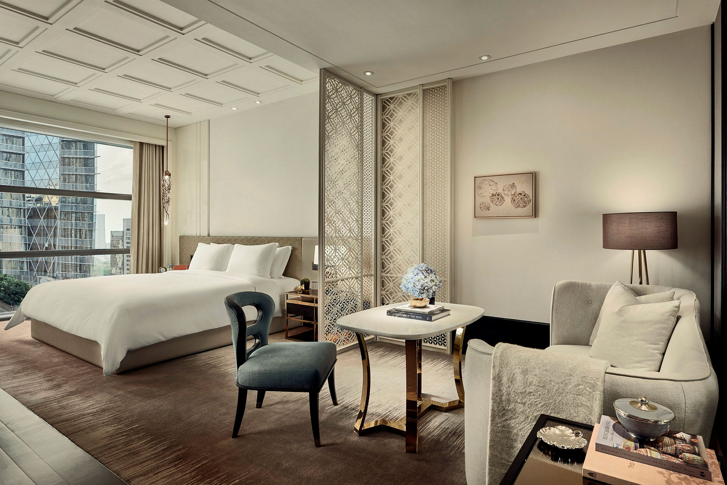 Ett elegant hotellrum med en stor säng, sittgrupp och fönster med utsikt över stadens byggnader. (AI-genererad text)