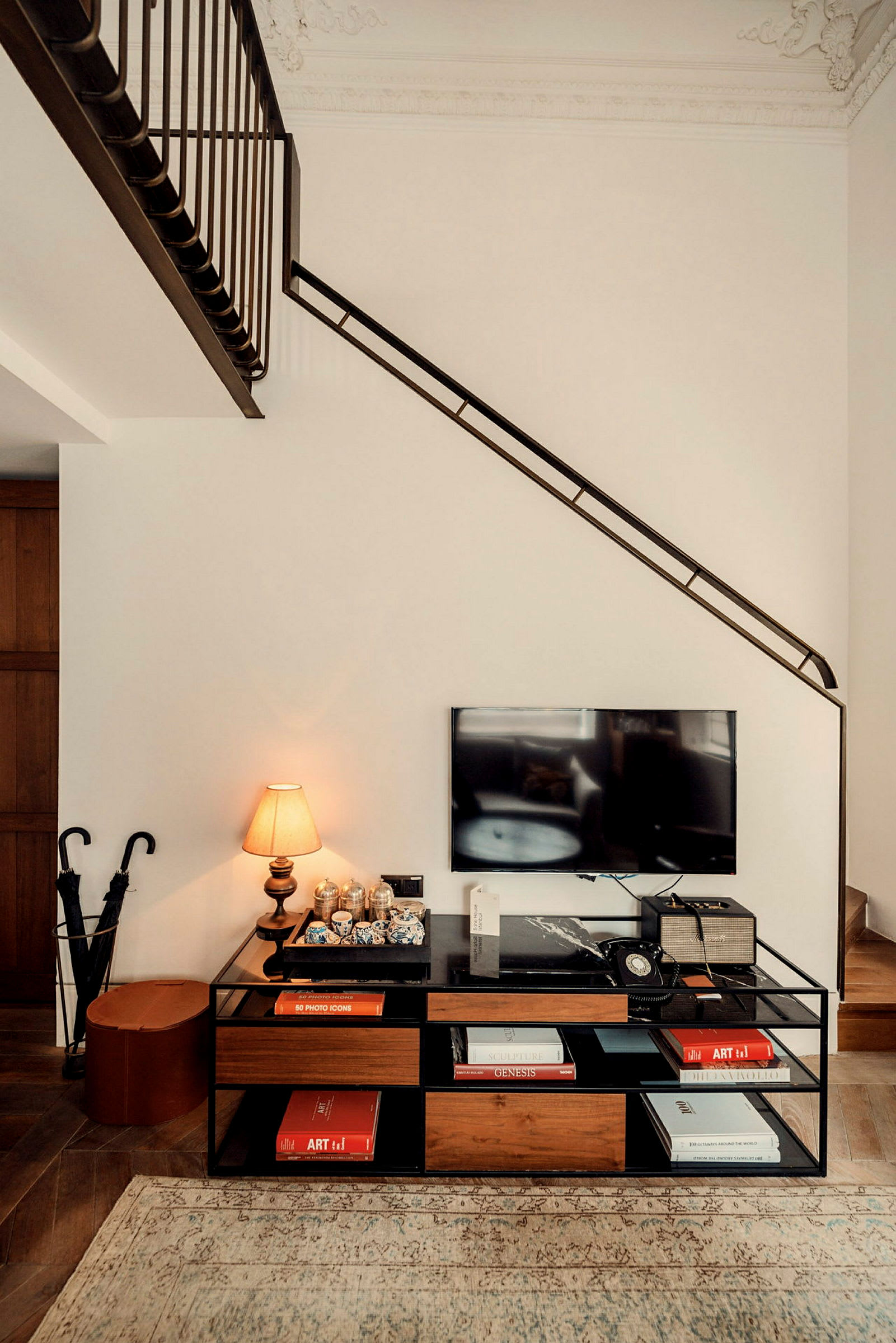 Interiör med en hylla som innehåller böcker, en bordslampa och dekorationer, en TV är monterad ovanför hyllan. (AI-genererad text)