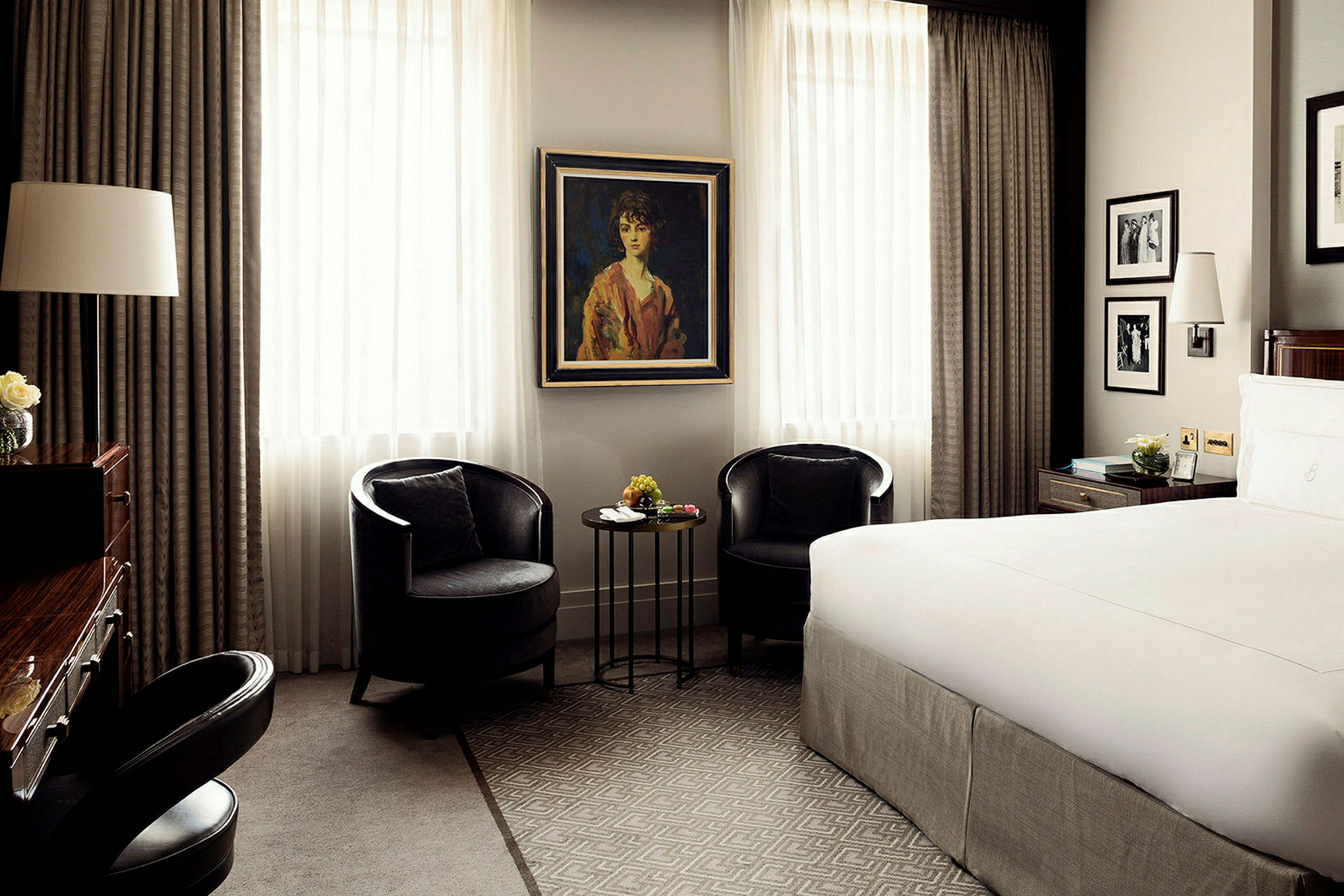 Elegant hotellrum med två svarta fåtöljer, ett litet bord med dekorationer och en stor säng. (AI-genererad text)