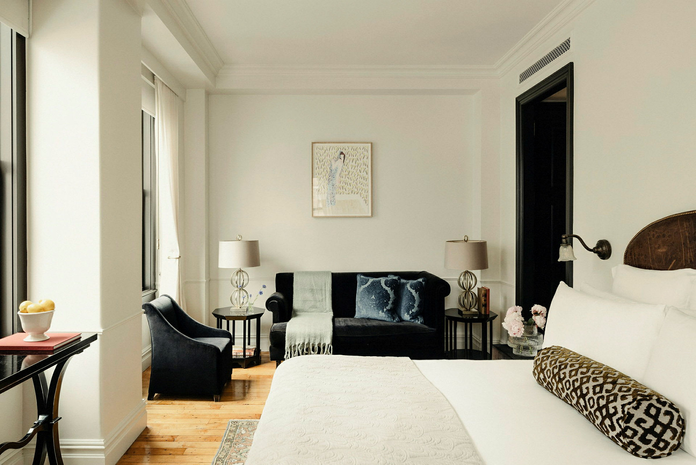 Hotellrum med en stor säng, en mörkblå soffa med kuddar och en fotölj samt sidobord med lampor. (AI-genererad text)