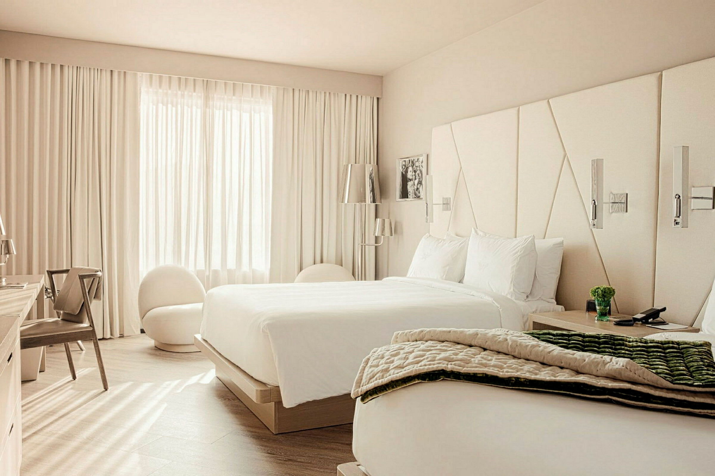 Ett hotellrum med två sängar, en stol och ett fönster med vita gardiner. (AI-genererad text)