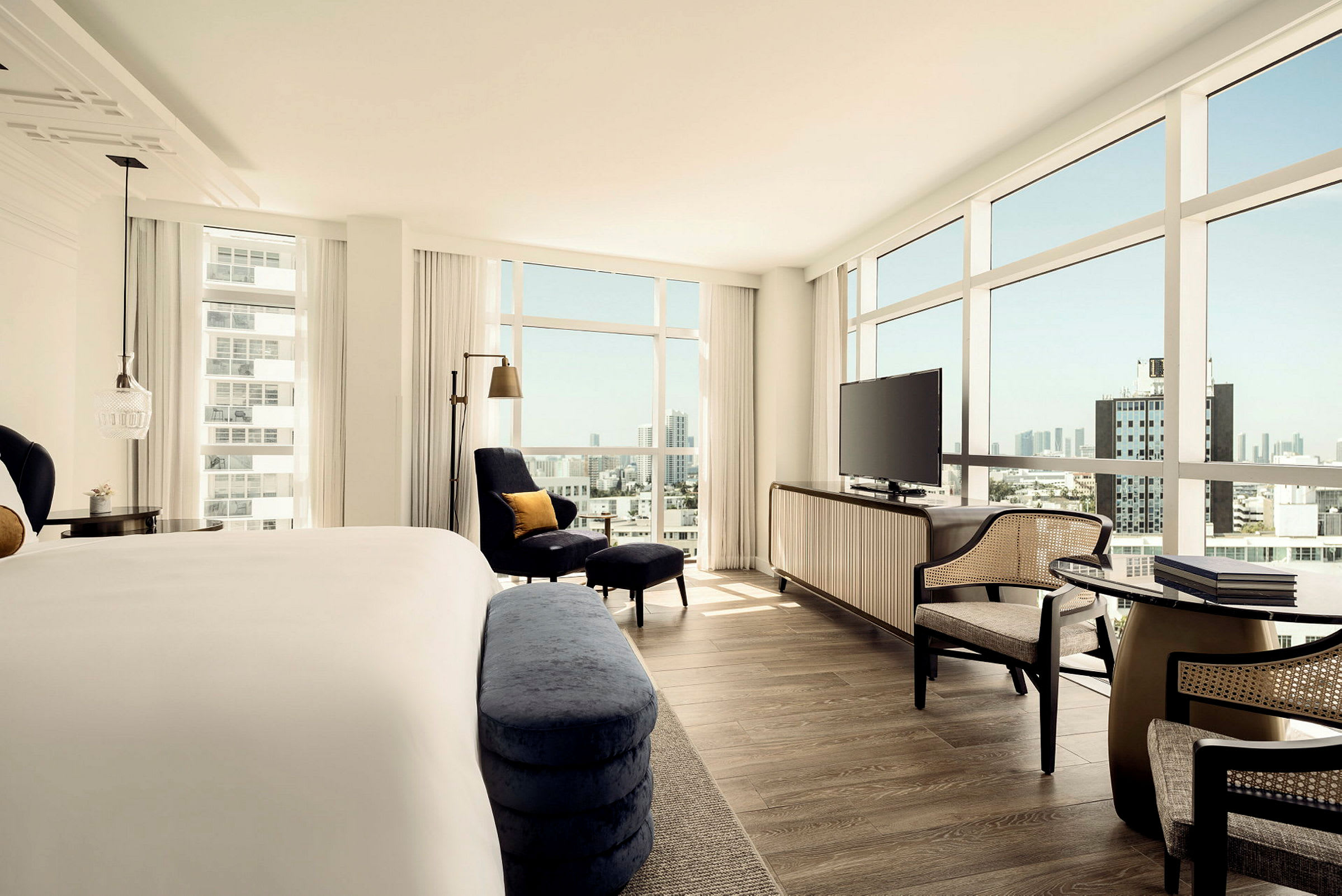 Hotellrum med säng, sittgrupp, en stor TV och stora fönster med utsikt över staden. (AI-genererad text)