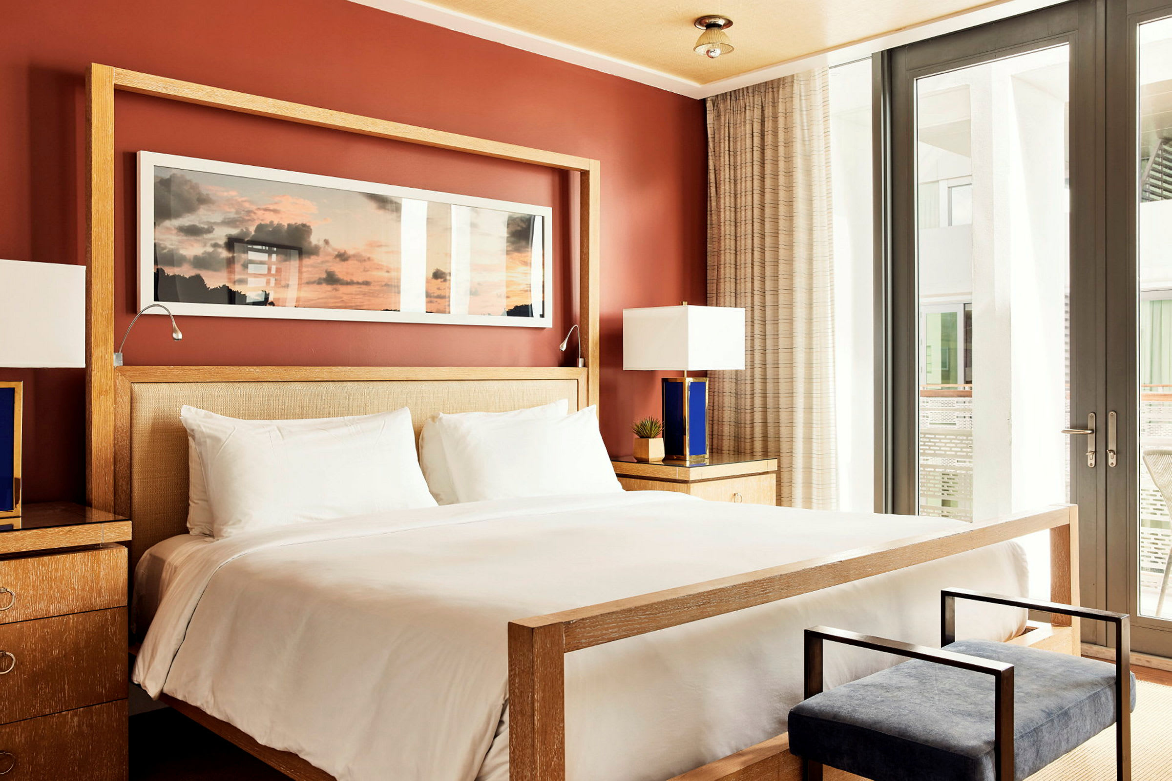 Ett stilfullt hotellrum med en stor säng, nattygsbord med lampor och en väggmålning ovanför sängen. (AI-genererad text)