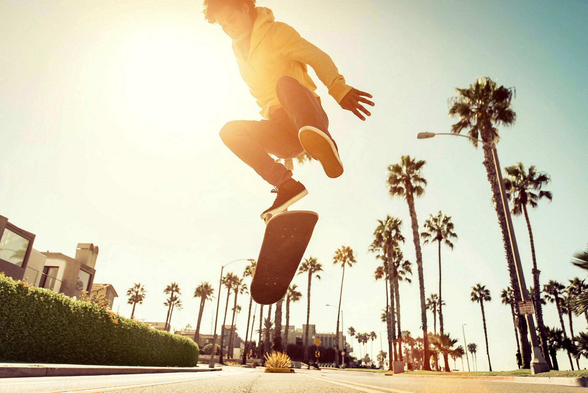 En person utför ett skateboardhopp på en gata kantad med palmer under solnedgång. (AI-genererad text)