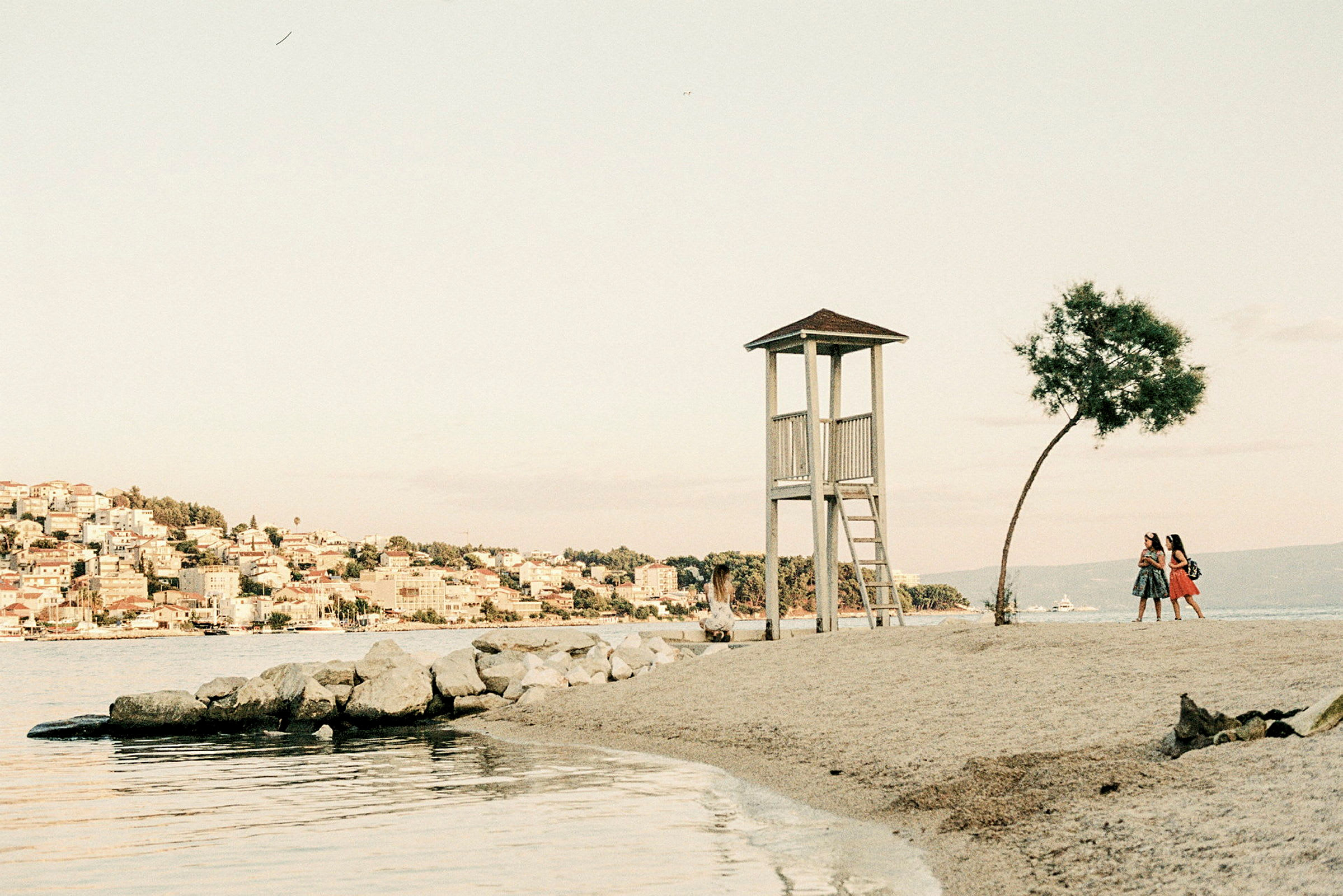 Vaktkur på en strand med två personer som promenerar nära ett träd. (AI-genererad text)