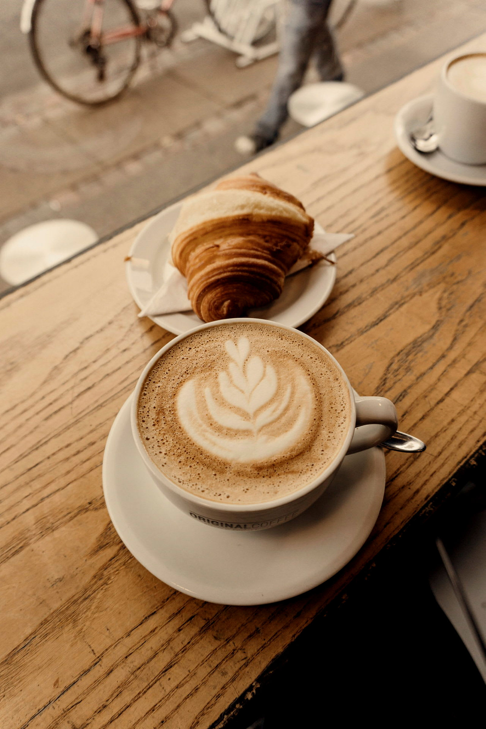 En kopp kaffe med latte-art och en croissant på ett bord. (AI-genererad text)