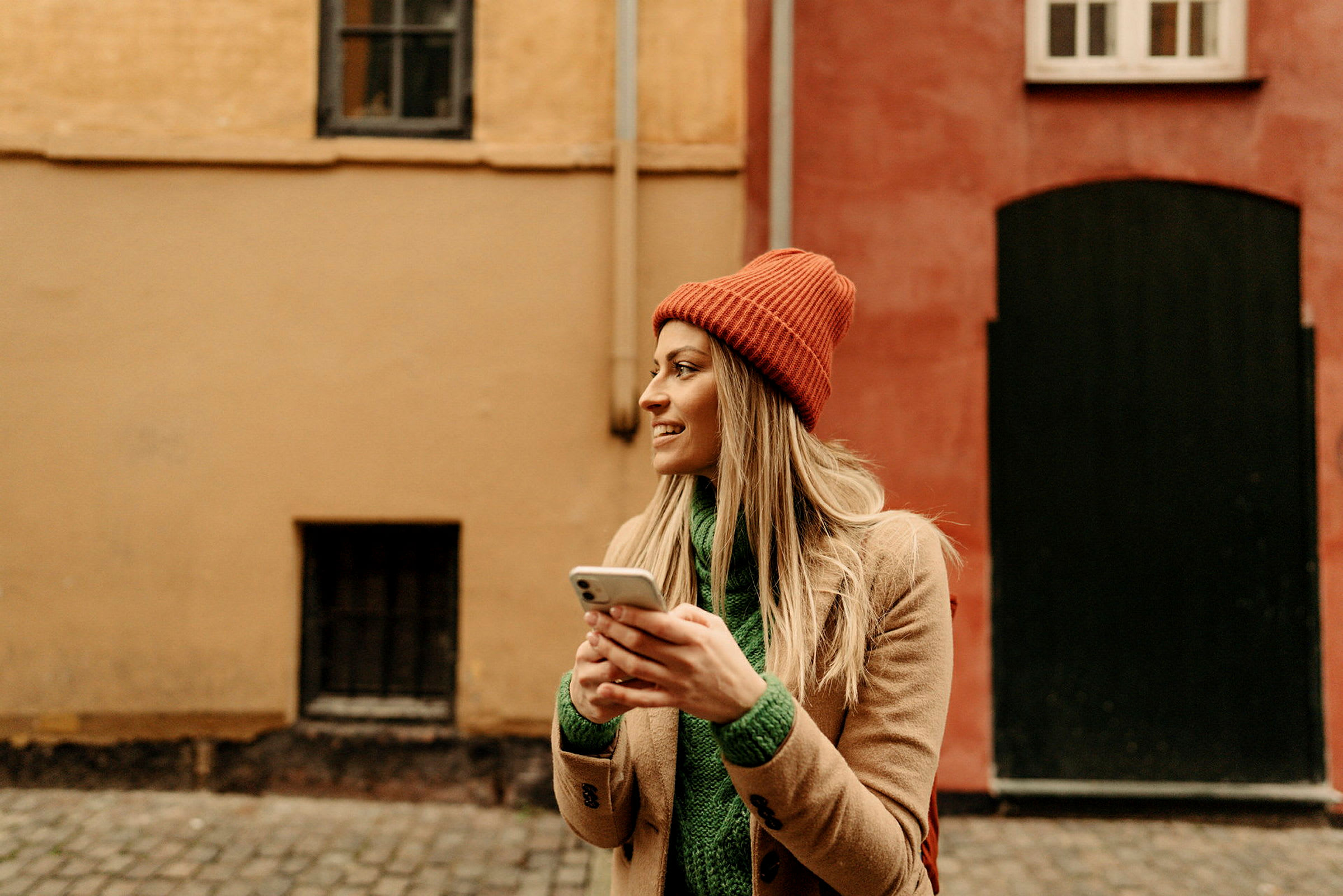 Person håller en mobiltelefon framför en färgglad byggnad. (AI-genererad text)