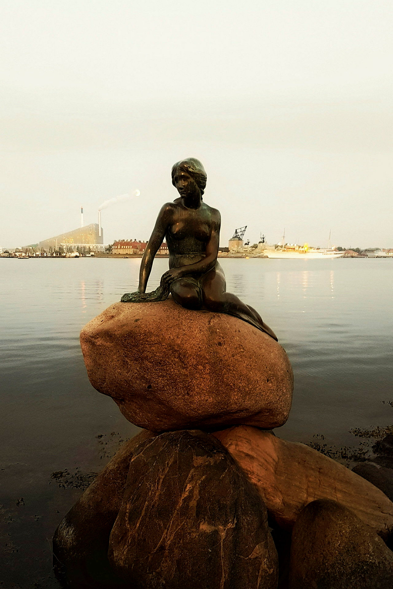 Statyn föreställer en sjöjungfru som sitter på en sten vid vattnet. (AI-genererad text)