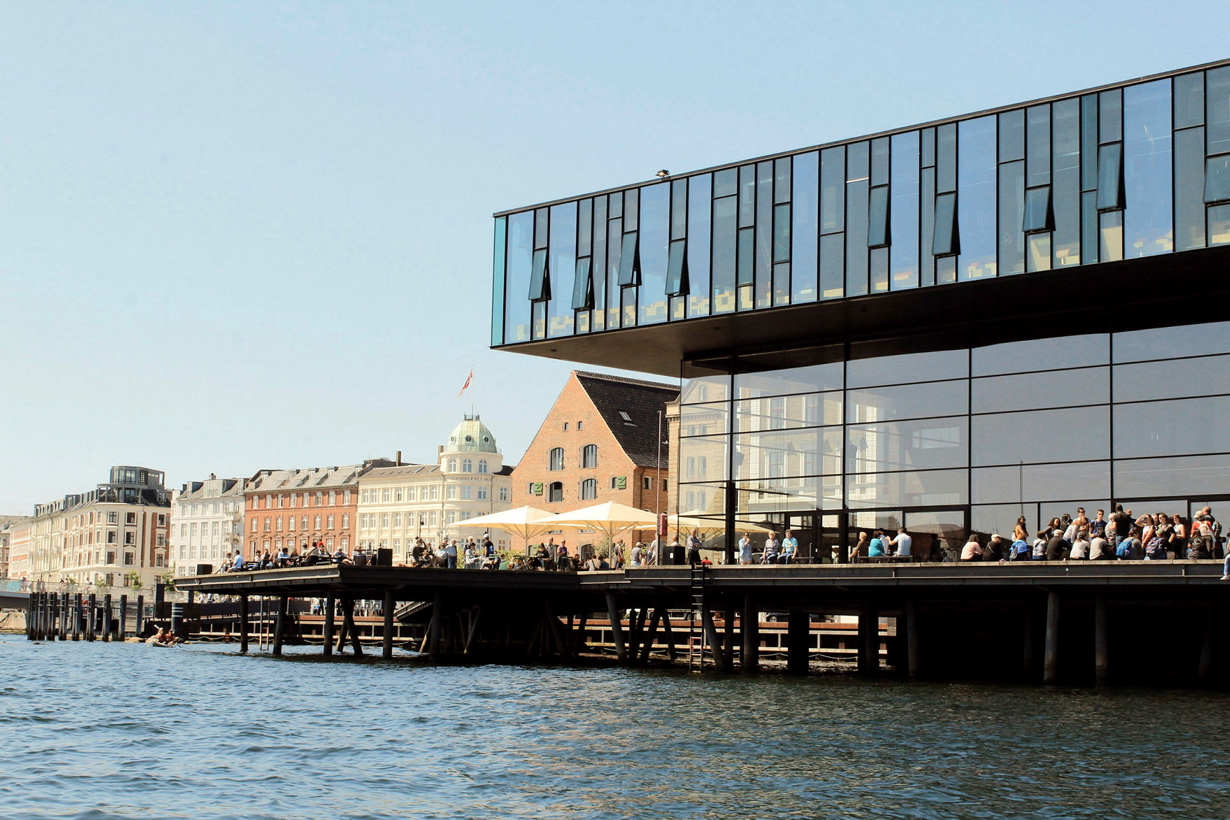 Folk samlade vid en modern byggnad intill en kanal. (AI-genererad text)