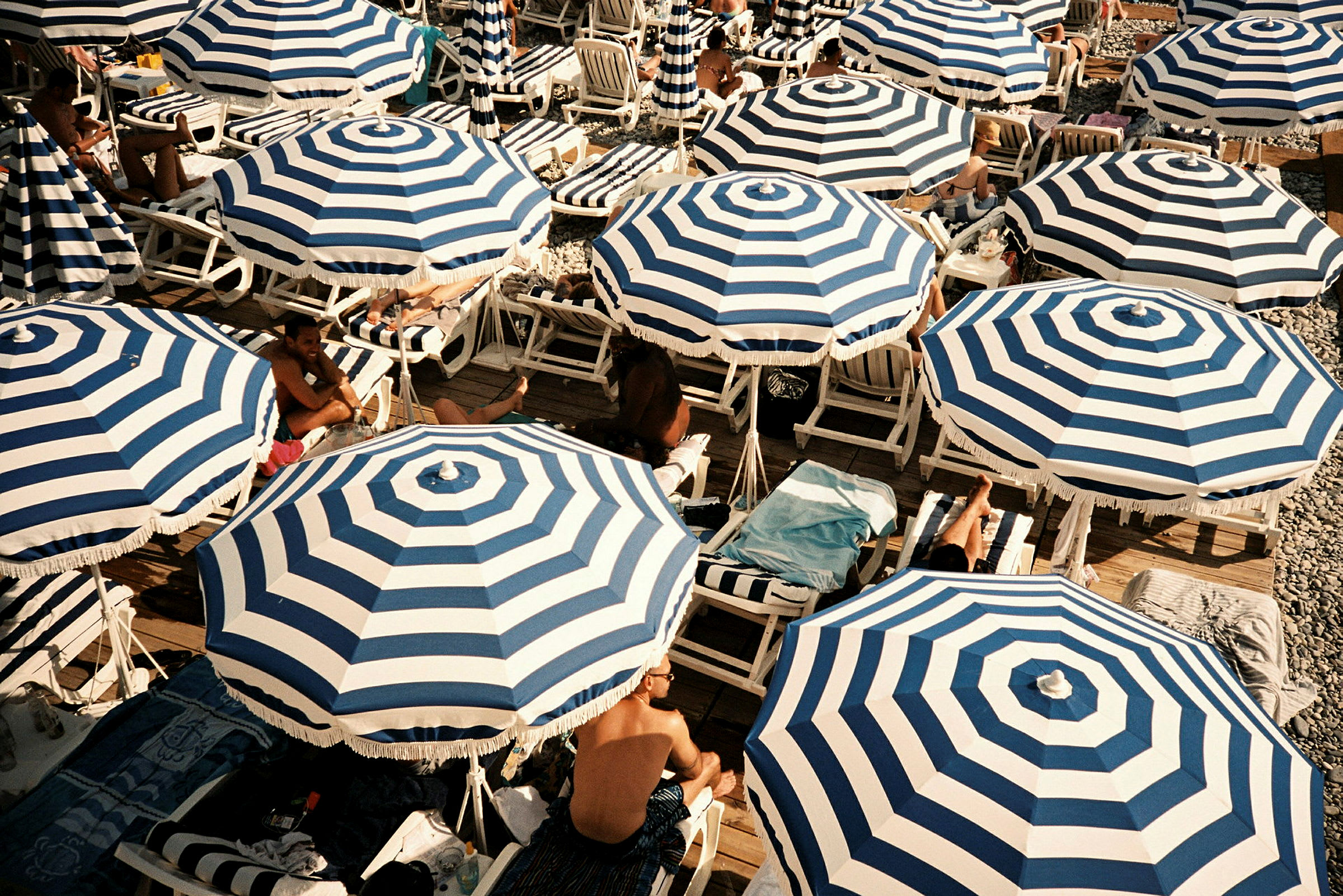 Strand med randiga blå och vita parasoller och solstolar. (AI-genererad text)