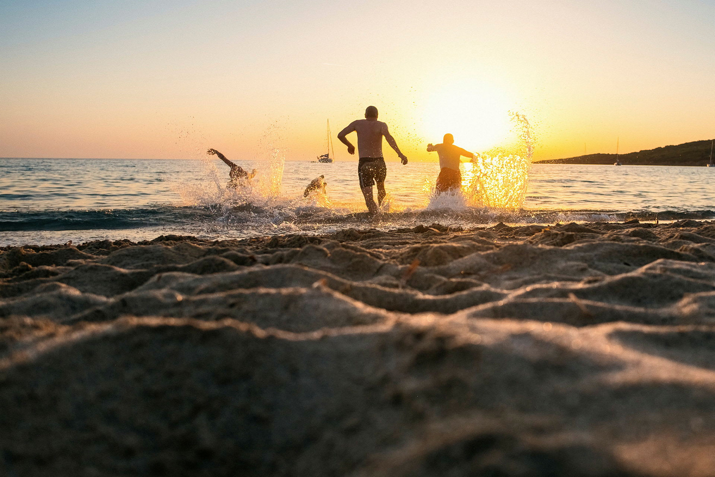 Personer springer i vattnet vid en strand under solnedgången. (AI-genererad text)