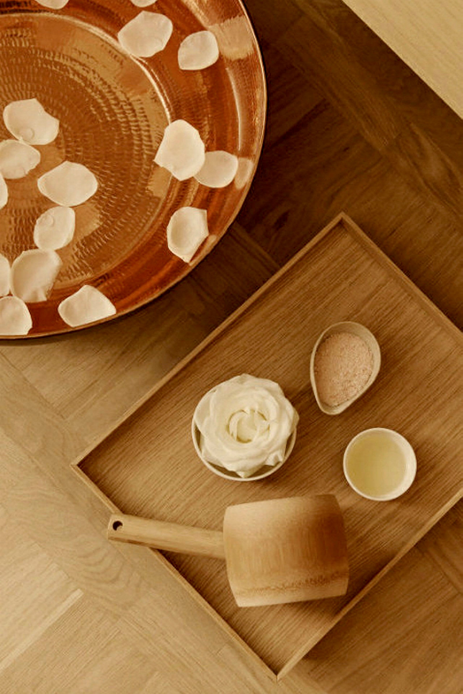 En trähink, en vit blomma, små skålar med ingredienser och en kopparbricka med rosenblad. (AI-genererad text)