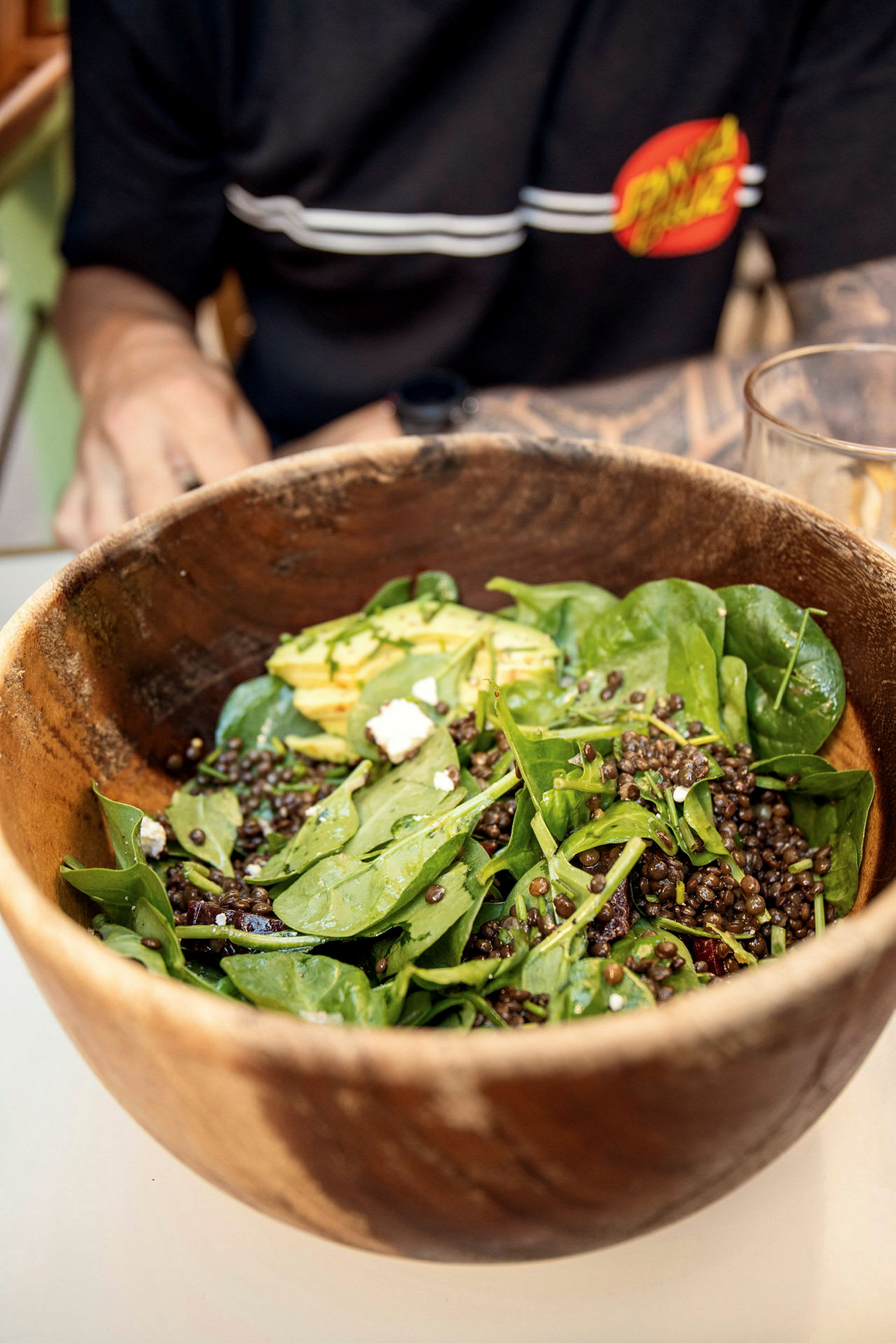 En träskål innehållande en sallad med bladgrönsaker, linser, avokado och fetaost. (AI-genererad text)