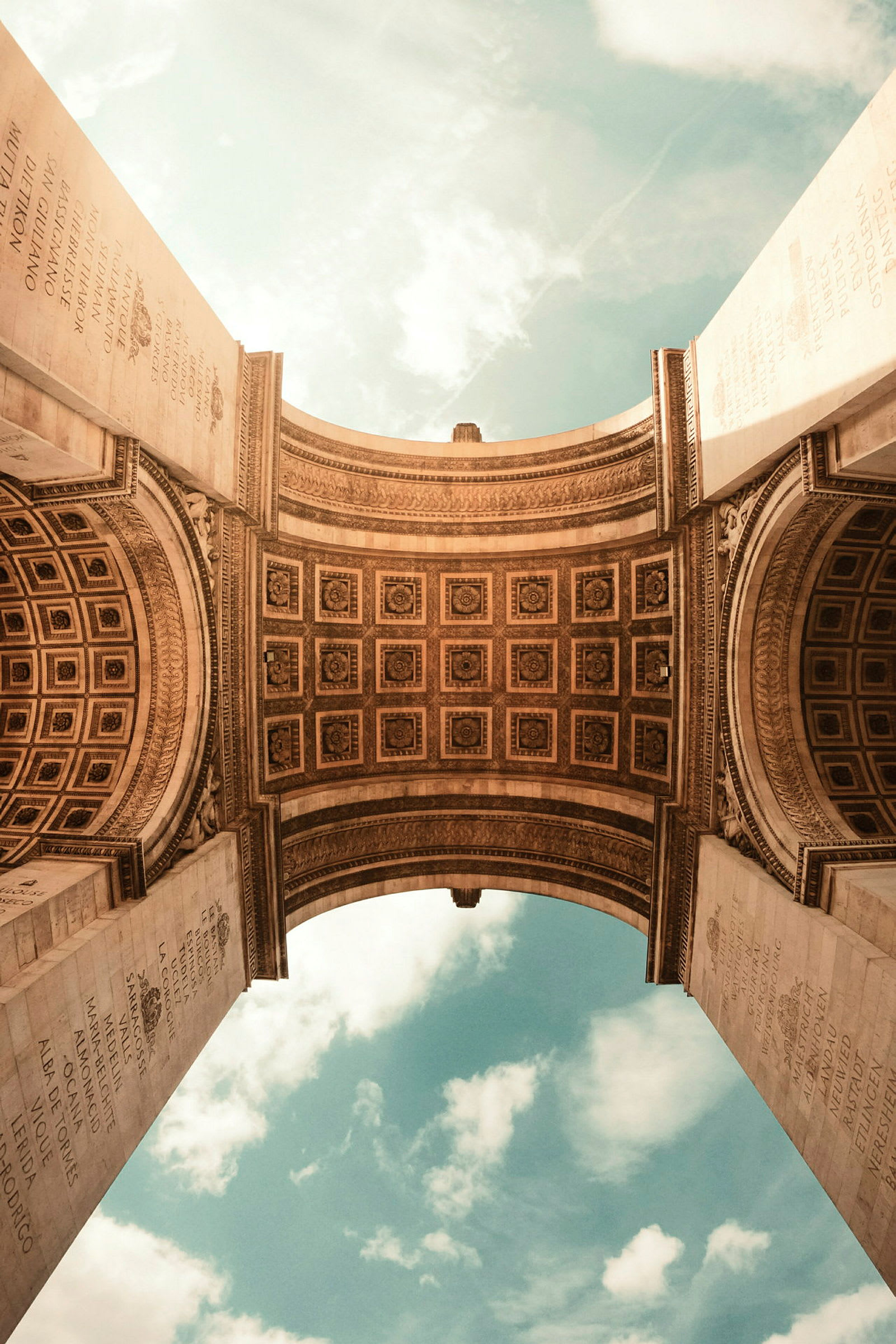 Vy mot valvet under Triumfbågen i Paris, med dekorerade ytor och en ljusblå himmel i bakgrunden. (AI-genererad text)