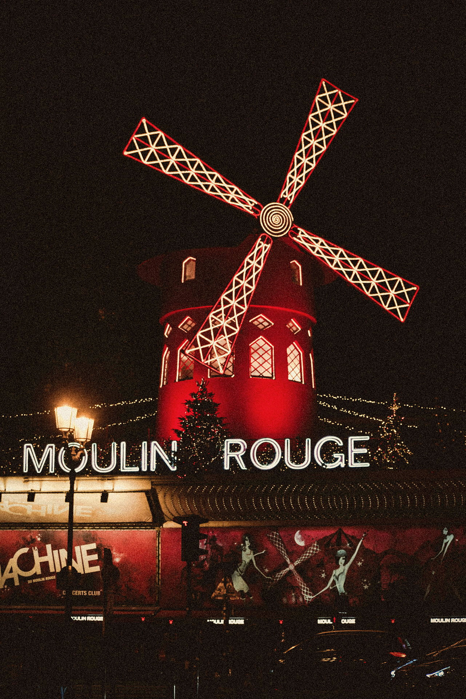 Bild av Moulin Rouge med sin röda väderkvarn och texten belyst mot natthimlen. (AI-genererad text)