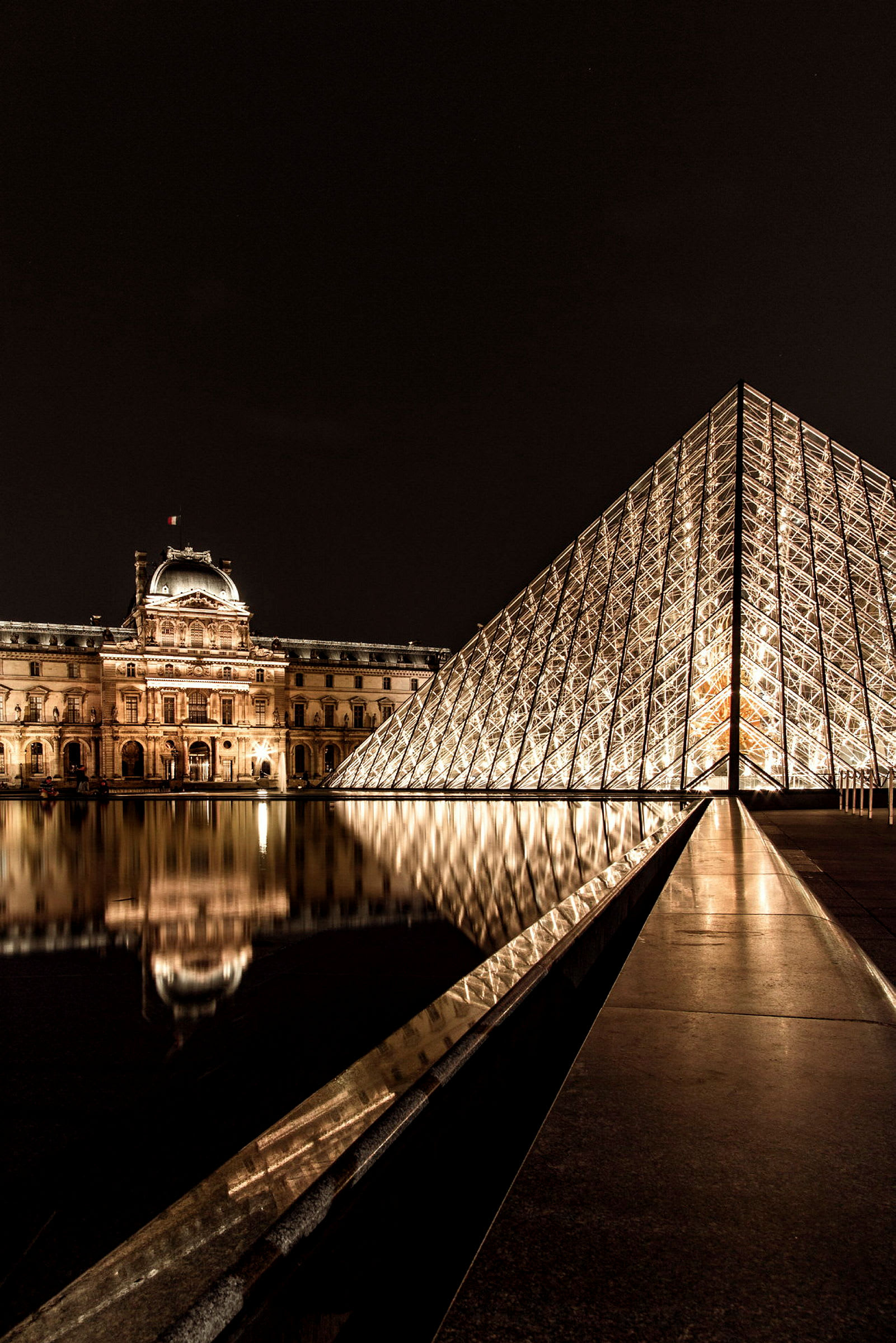Bildens föreställer Louvren i Paris och dess glas-pyramid belyst på natten. (AI-genererad text)