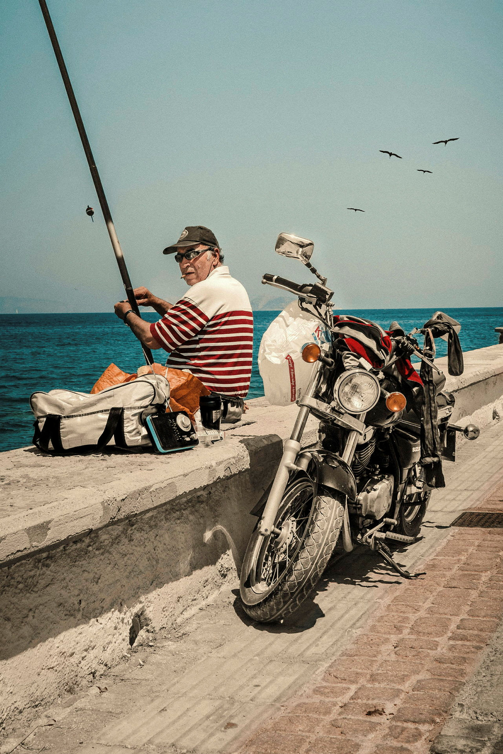 En person fiskar vid en kaj, med en motorcykel parkerad bredvid sig. (AI-genererad text)