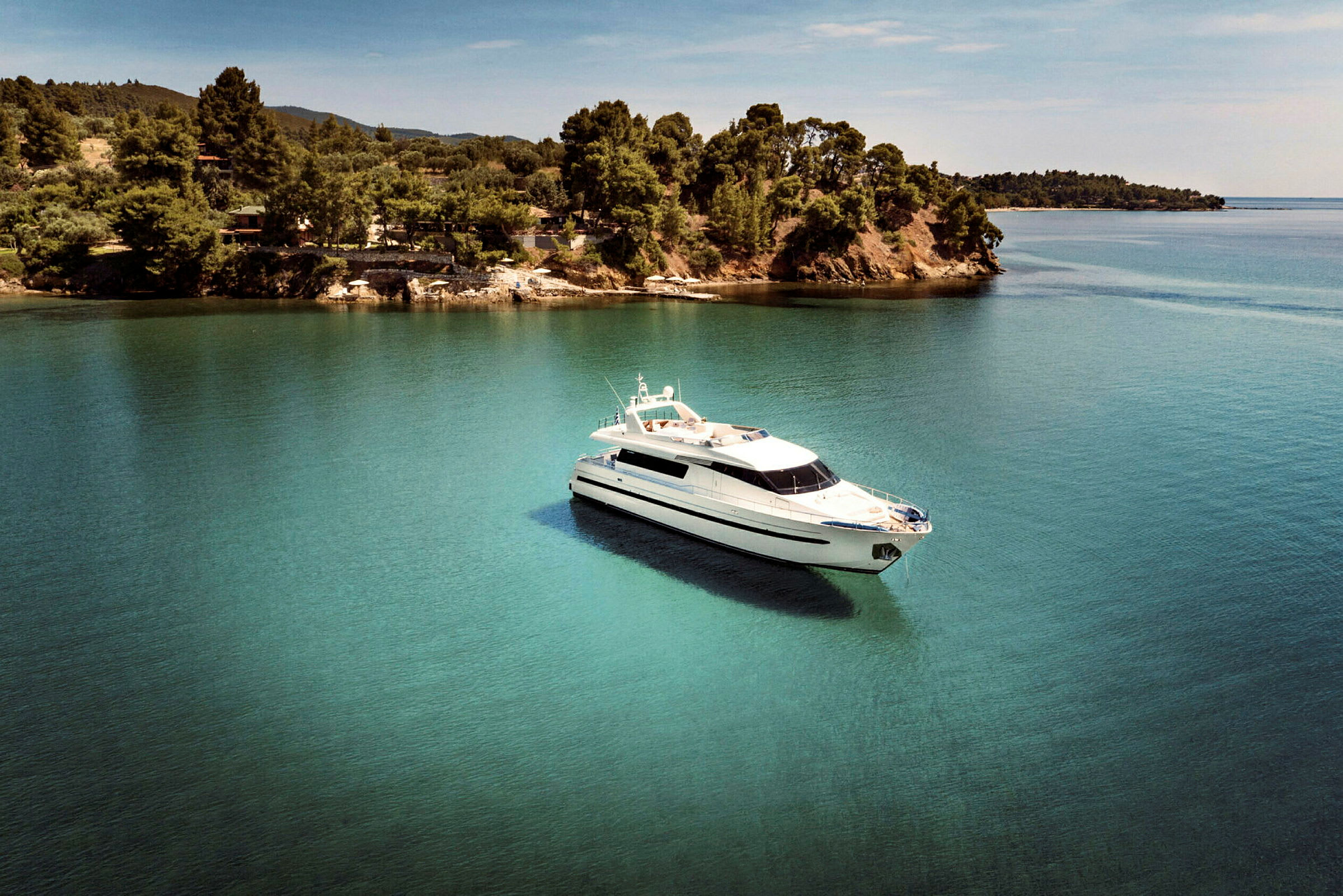 En vit yacht flyter på klart vatten nära en grönskande kust. (AI-genererad text)
