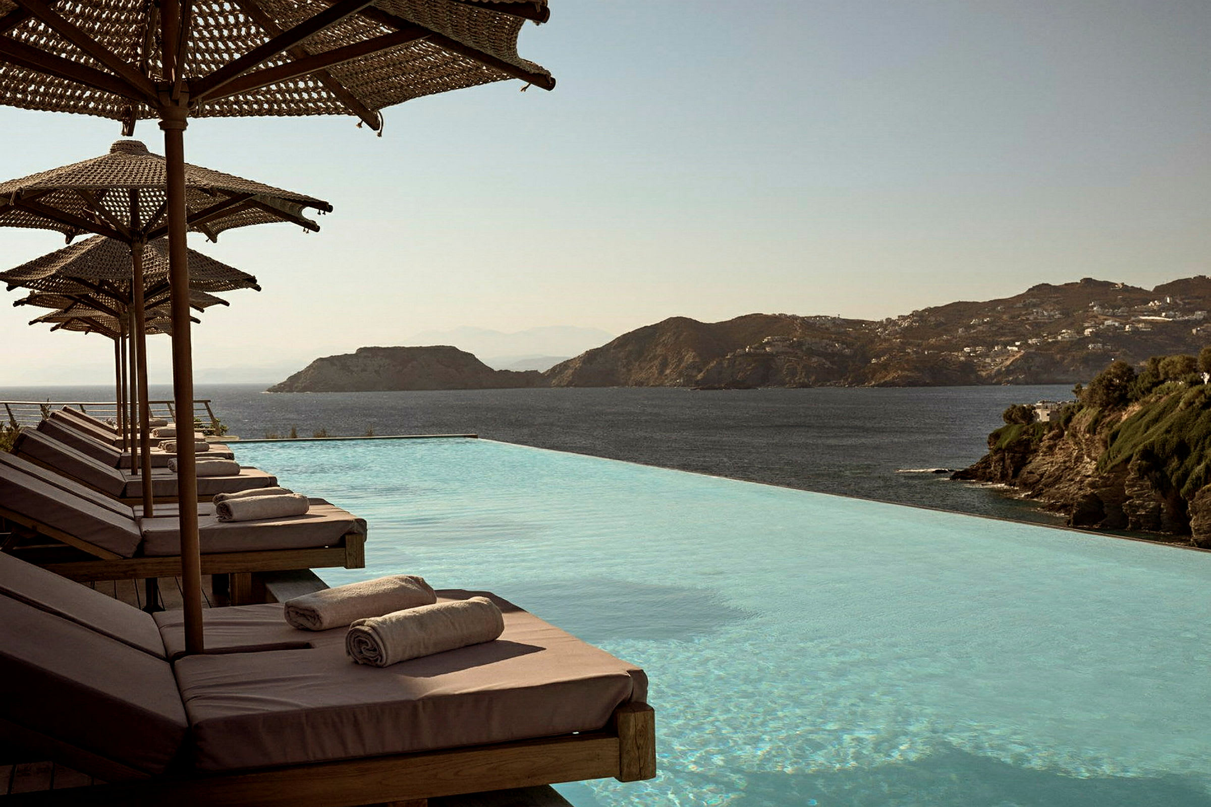 Solstolar med handdukar vid en infinitypool med havsutsikt. (AI-genererad text)