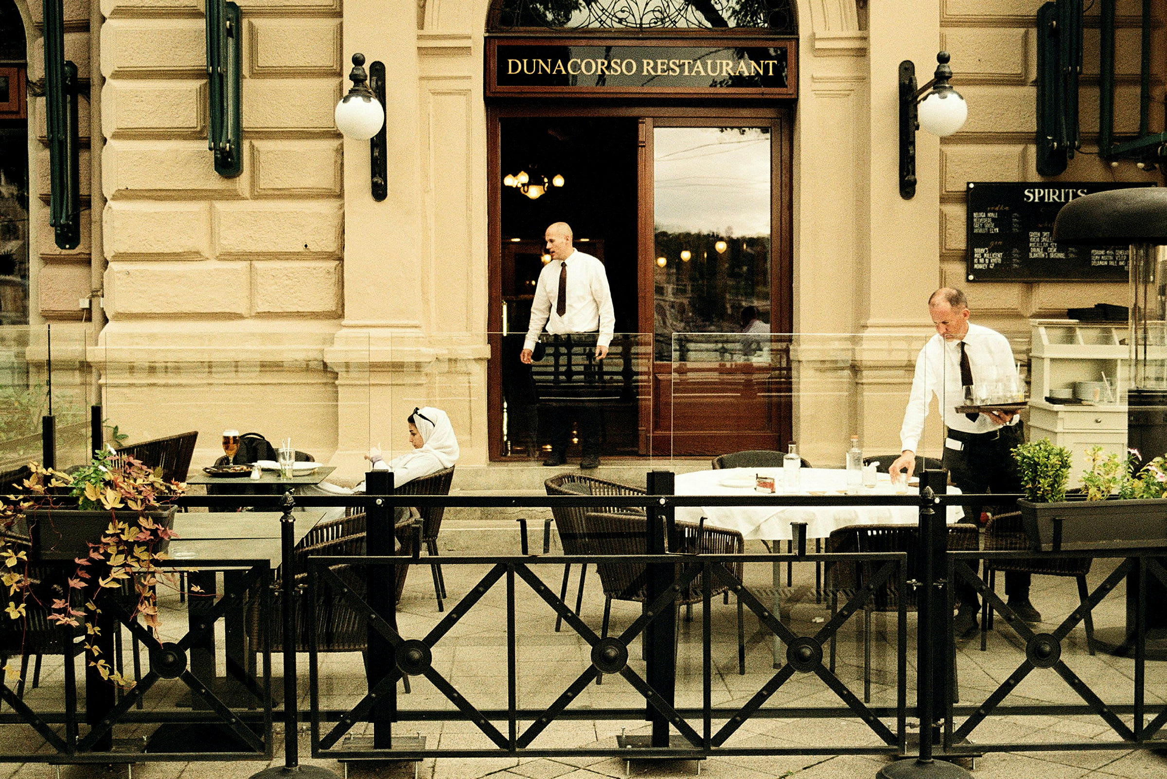 Utomhusbord vid restaurangen Dunacorso med byggnadsfasad och glasfront. (AI-genererad text)