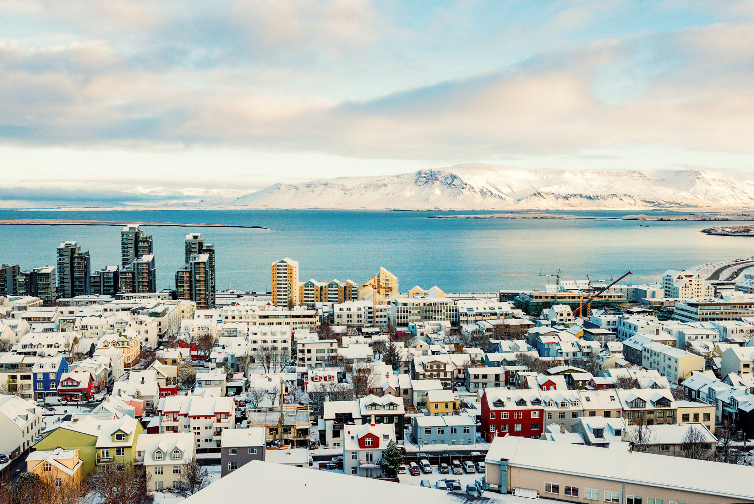 En stad vid havet med snötäckta byggnader och fjäll i bakgrunden. (AI-genererad text)