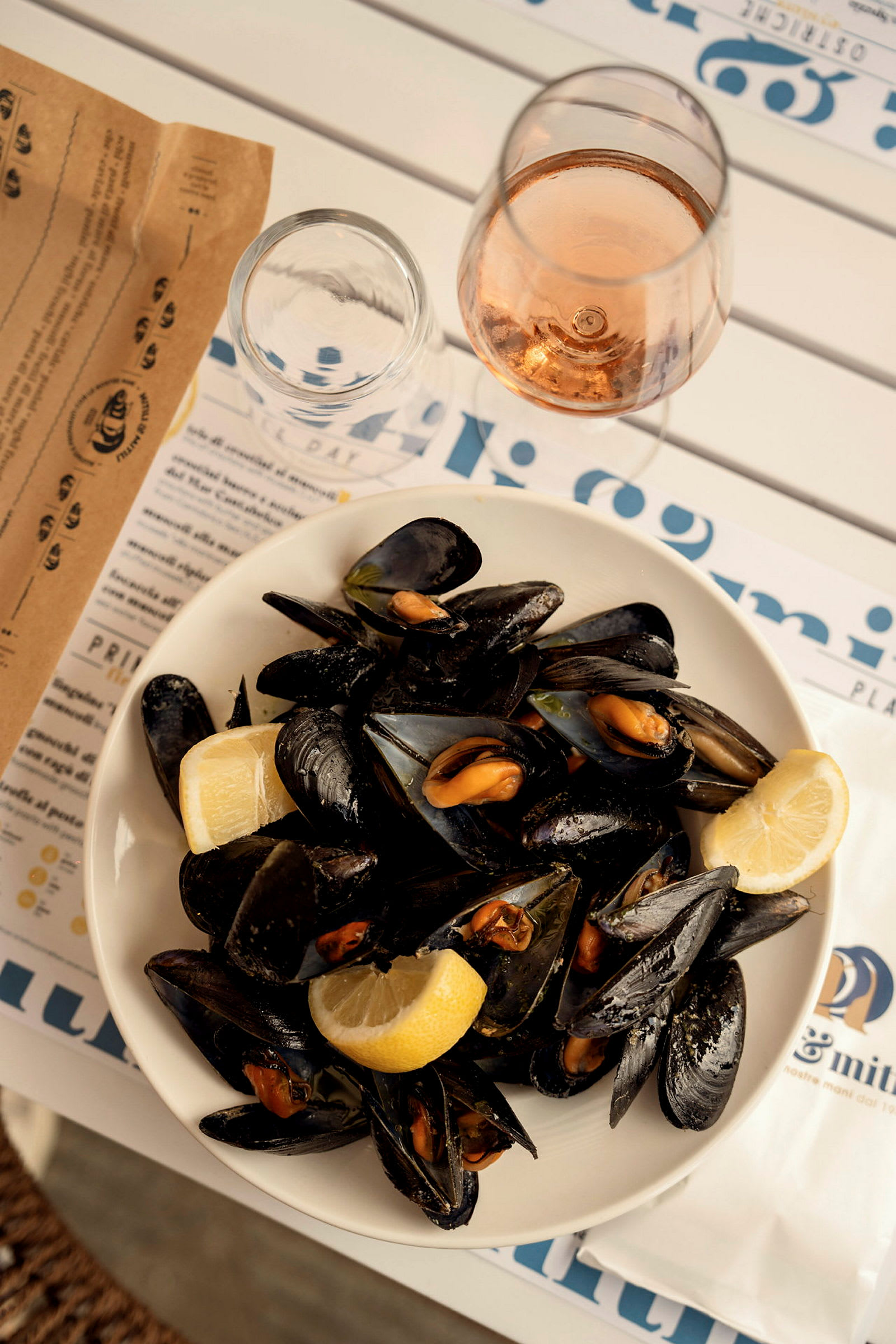 En tallrik med kokta musslor och citronskivor, serverad på ett bord med ett glas vin. (AI-genererad text)