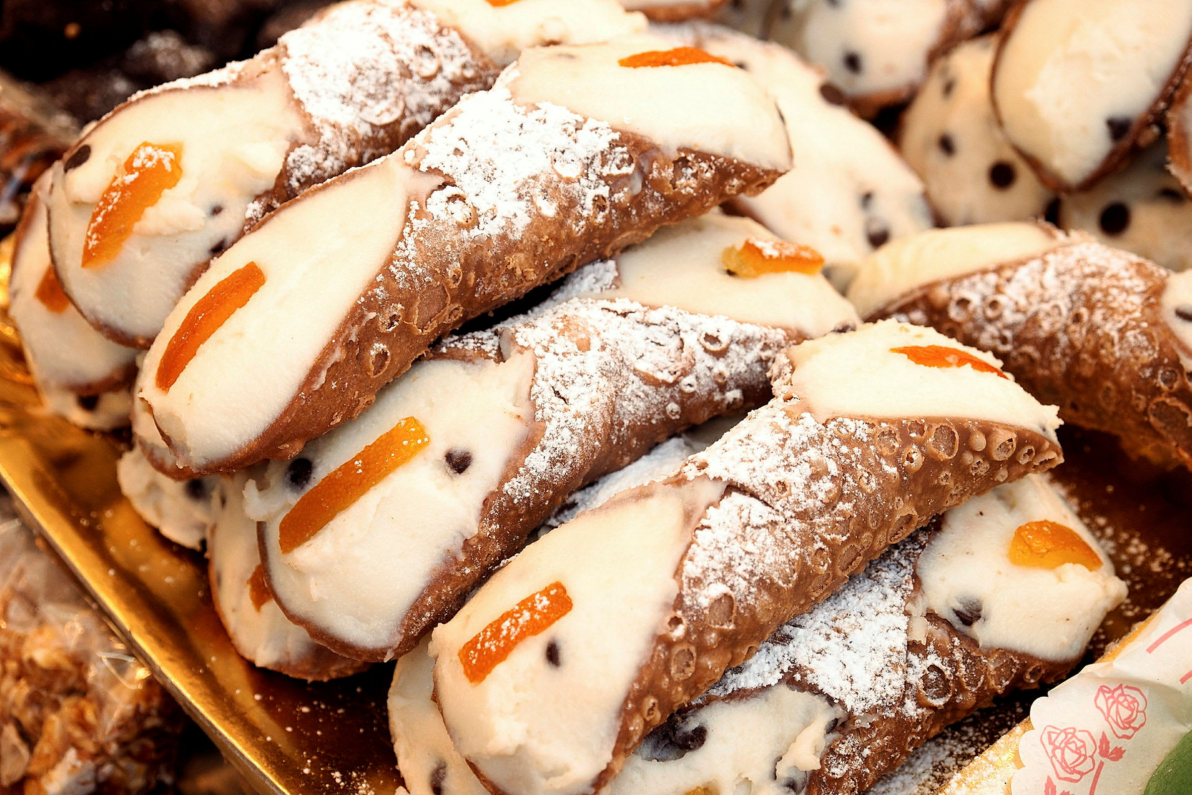 Cannoli på en bricka, fyllda med kräm och dekorerade med pudrat florsocker och apelsinskal. (AI-genererad text)