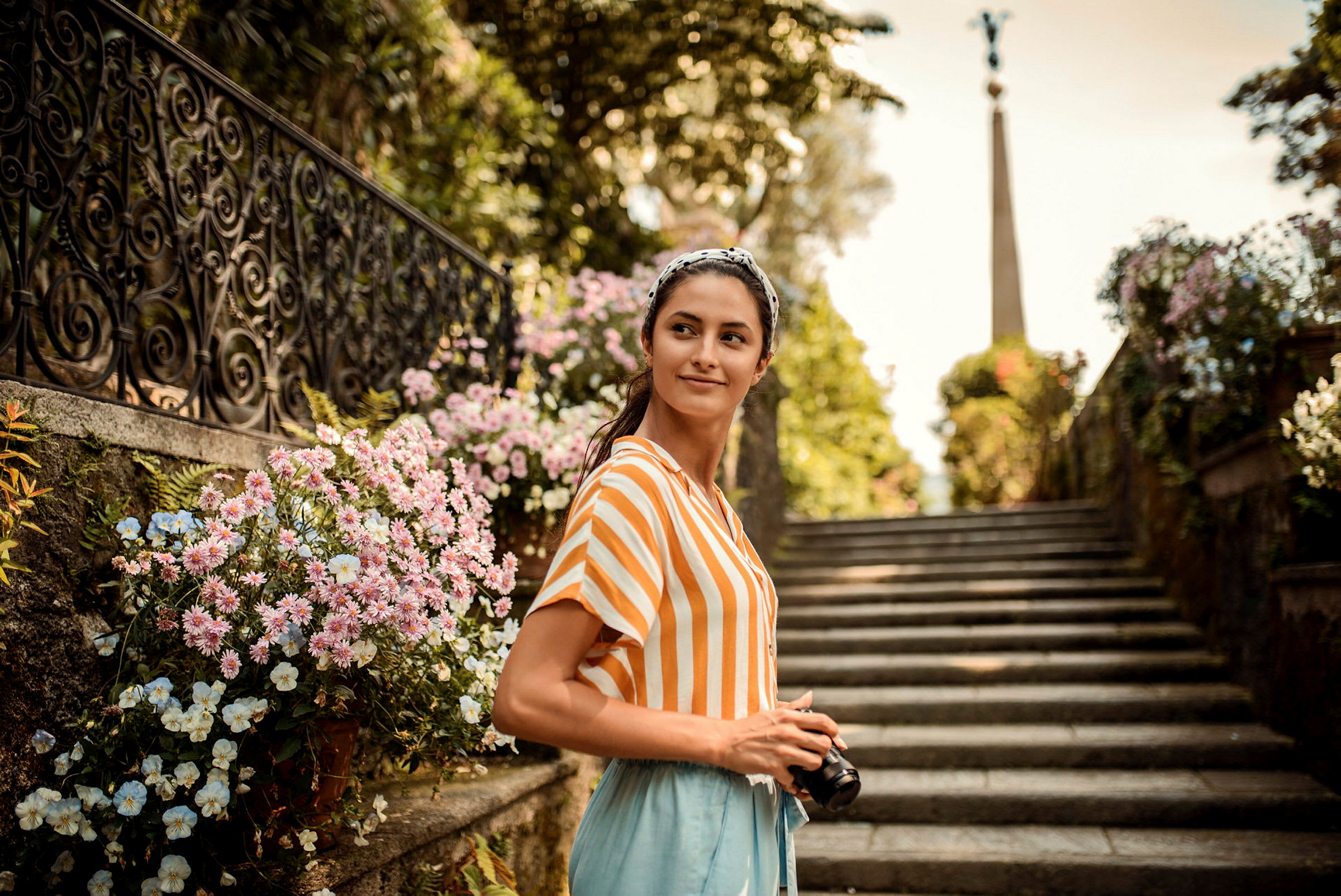 En person håller en kamera vid en blomsterkantad trappa. (AI-genererad text)