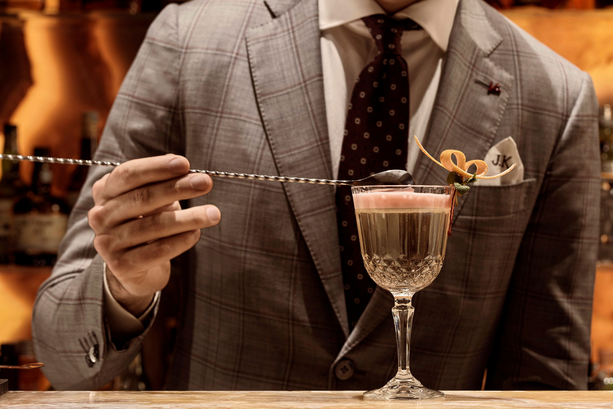 En man i kostym håller i en sked över ett cocktailglas. (AI-genererad text)