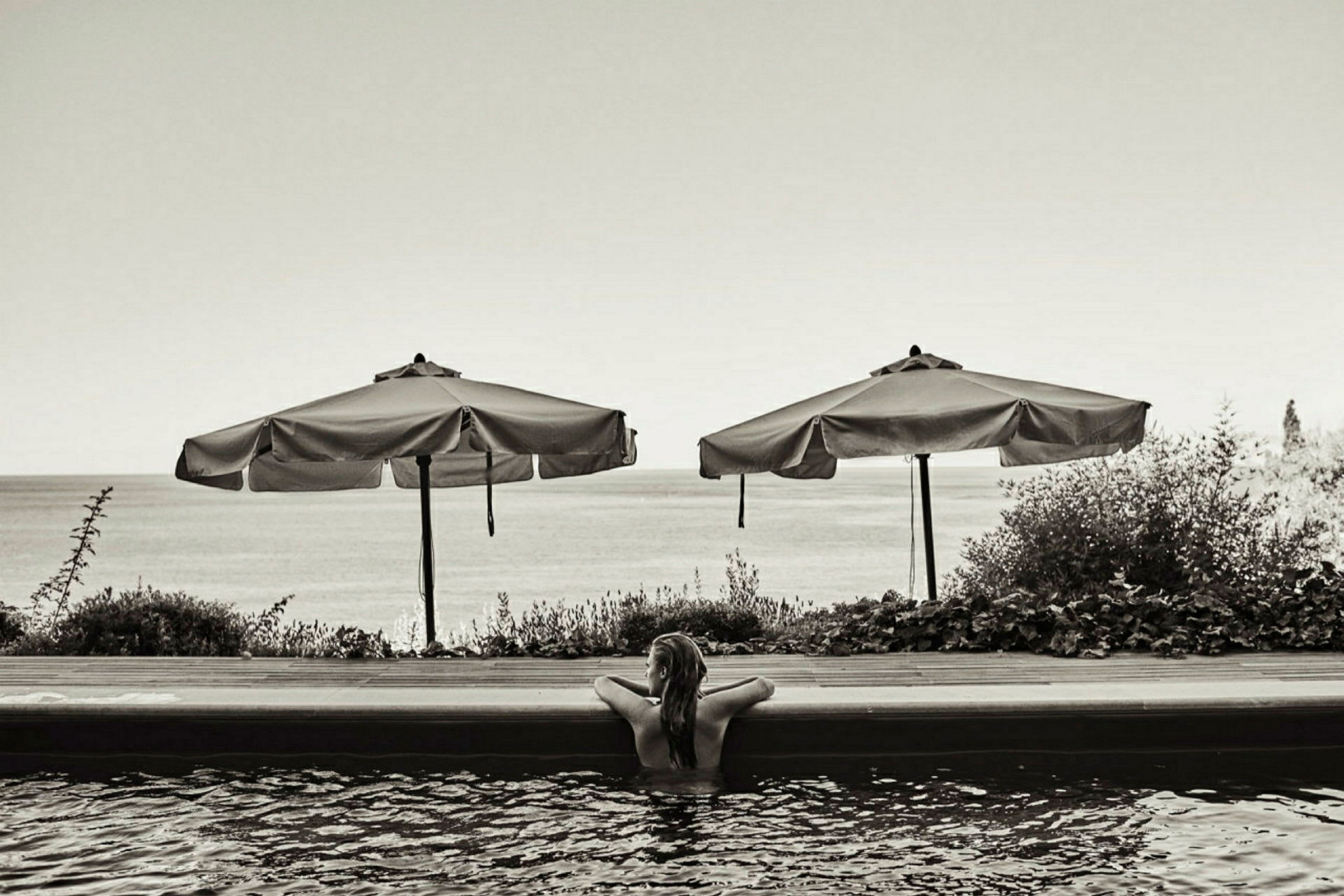 Person i pool med parasoller och havet i bakgrunden. (AI-genererad text)