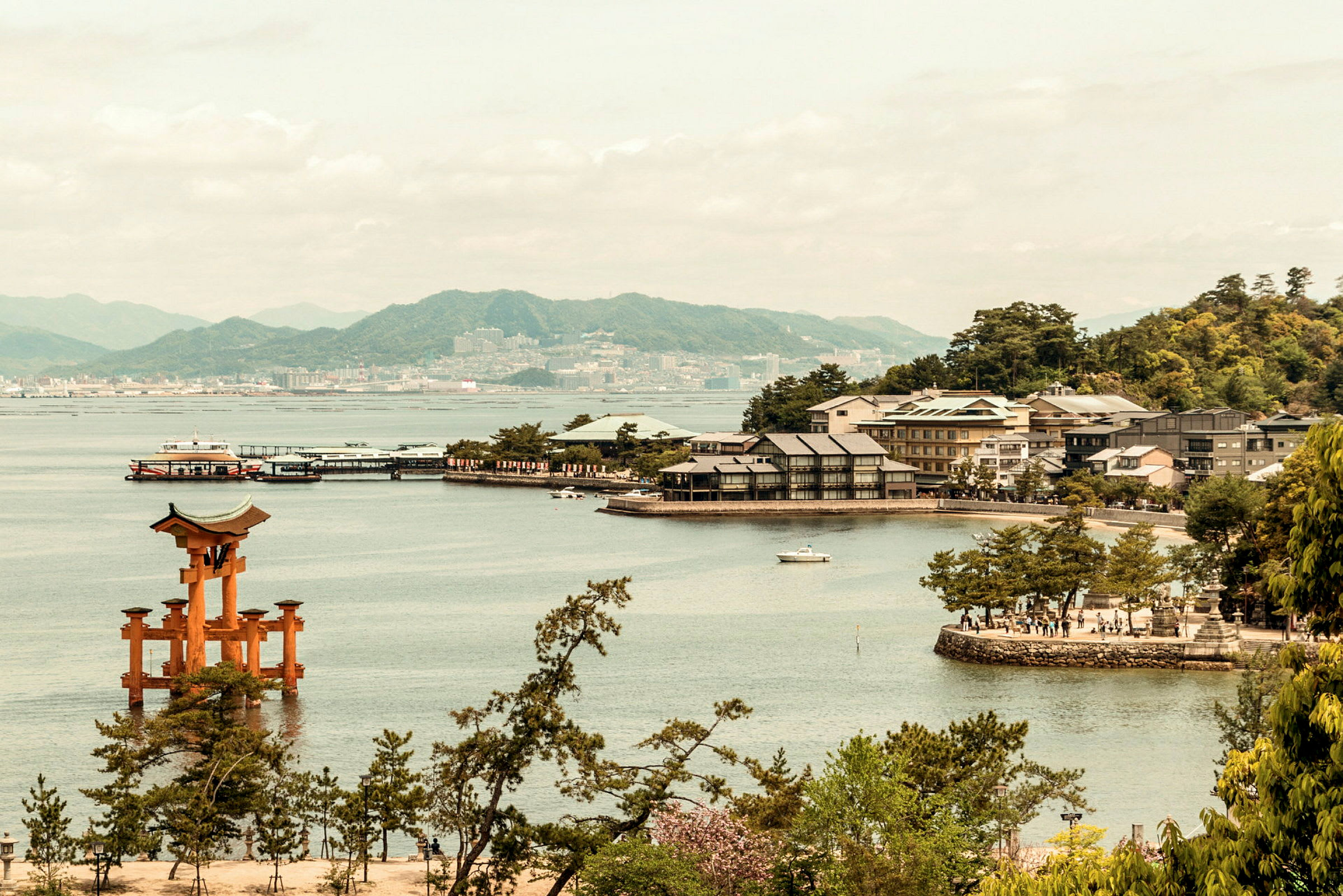 Bild av ett kustlandskap med en traditionell japansk toriiport i vattnet, byggnader vid stranden och berg i bakgrunden. (AI-genererad text)